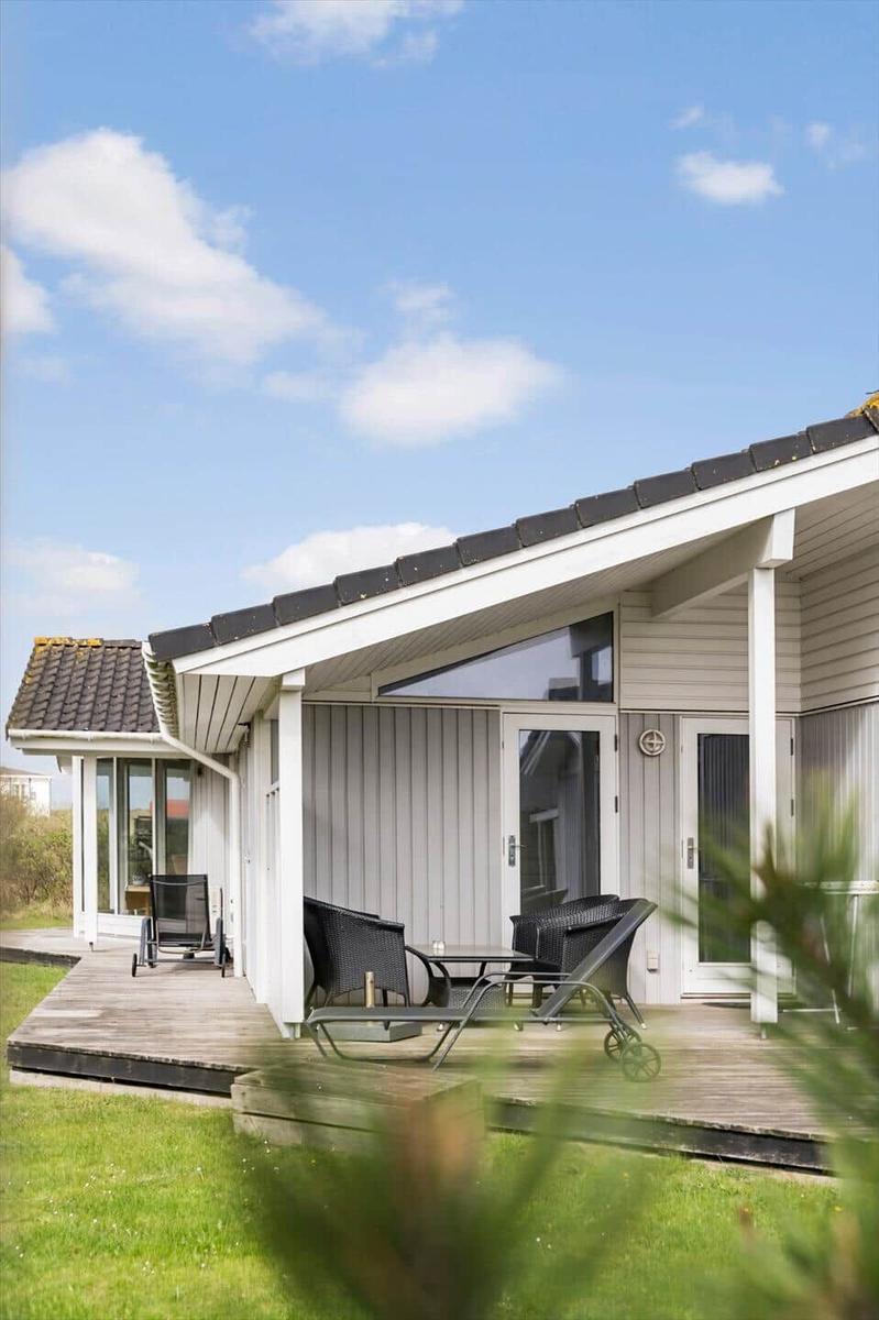 Moderne Ferienhaus mit Terrasse, Garten und Sitzgelegenheiten unter blauem Himmel.