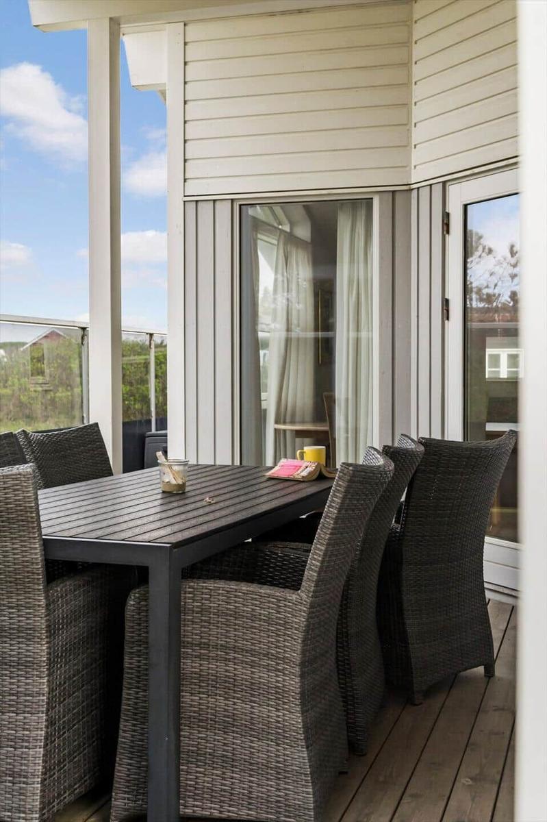 Terrasse mit Esstisch und Stühlen, Blick auf Garten und Himmel.