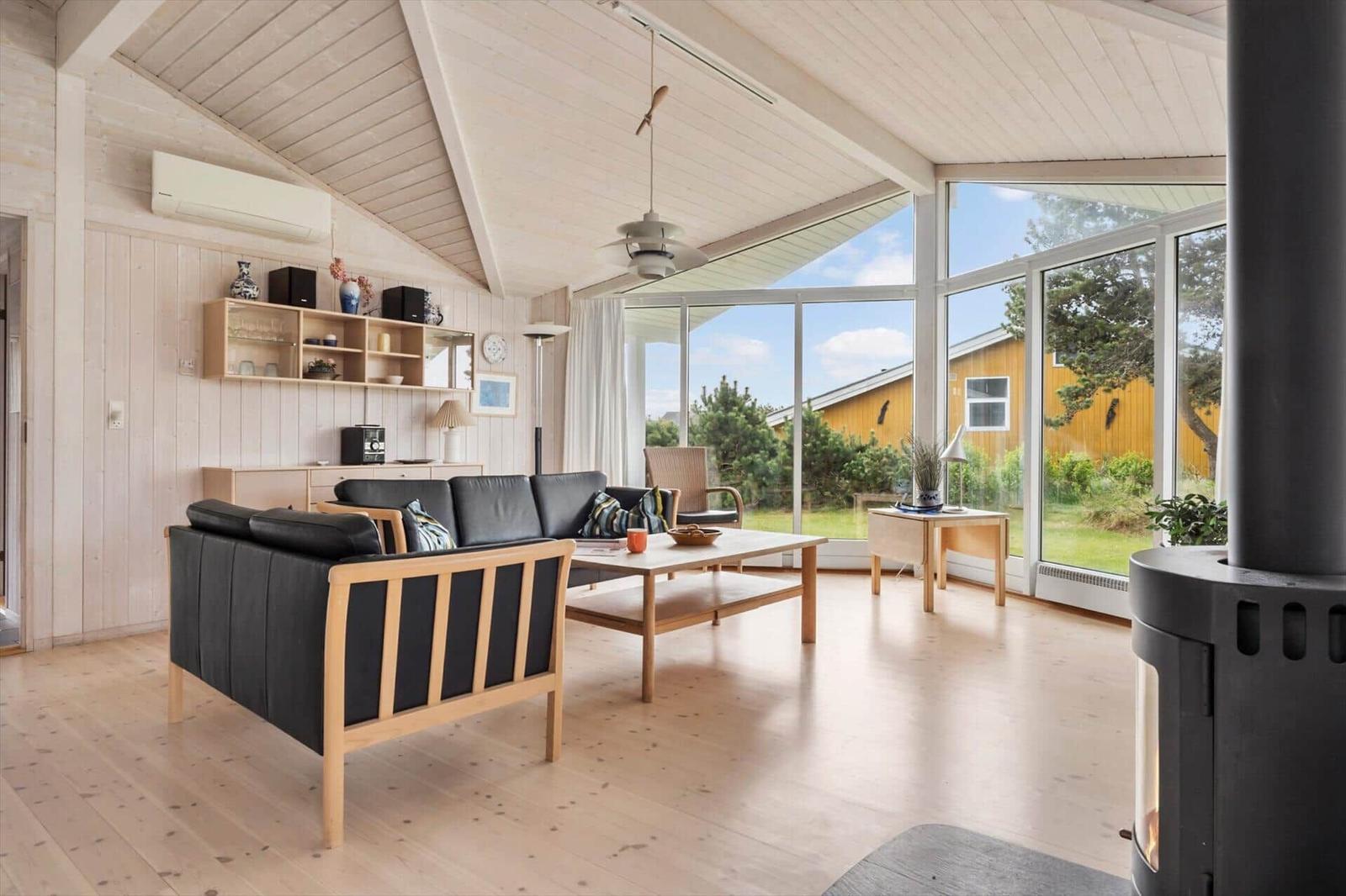 Wohnzimmer mit Holzboden, schwarzen Sofas und großen Fenstern zum Garten.
