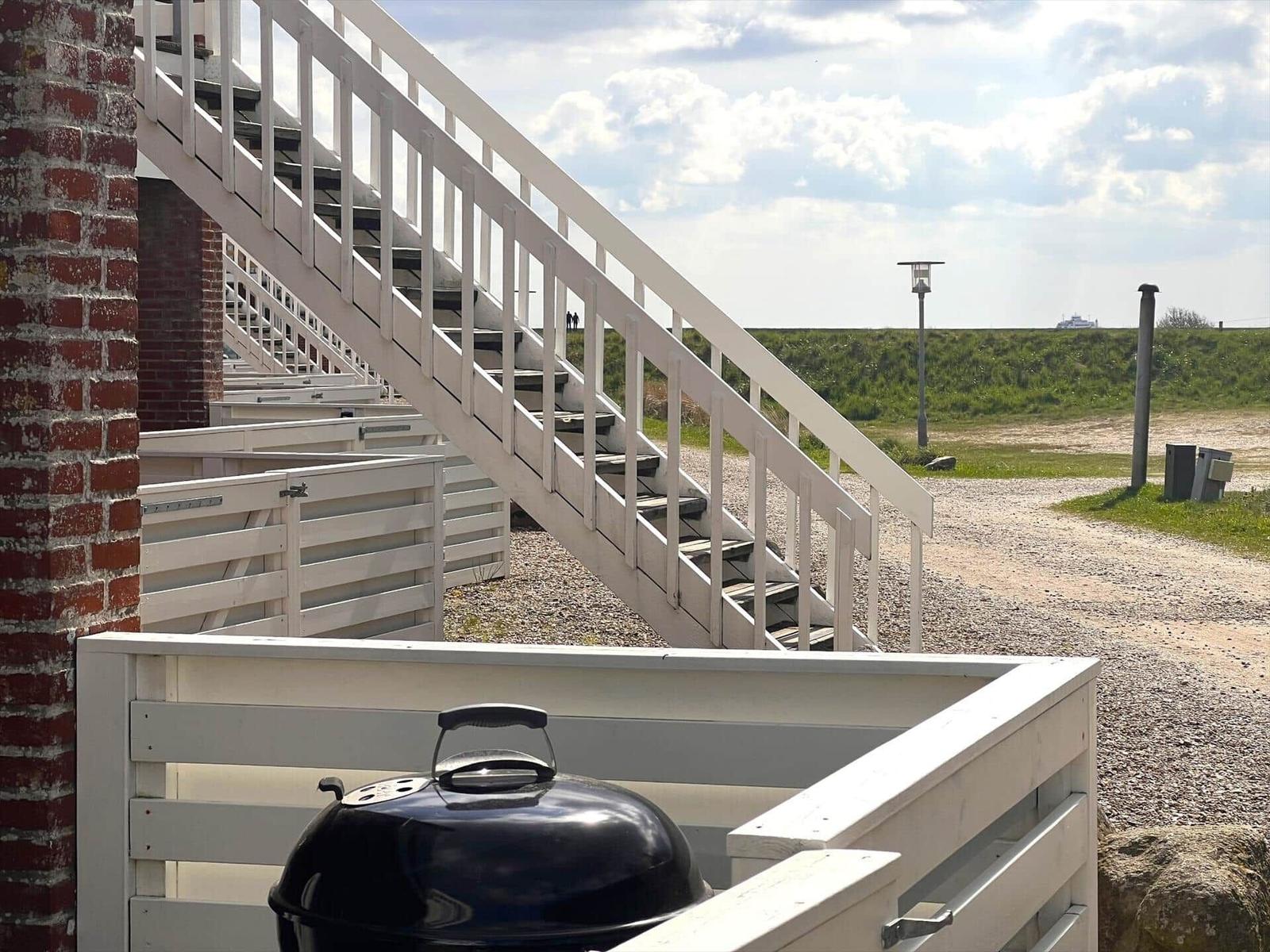 Außenbereich mit Grill, weißen Stufen und Blick auf Grünfläche.