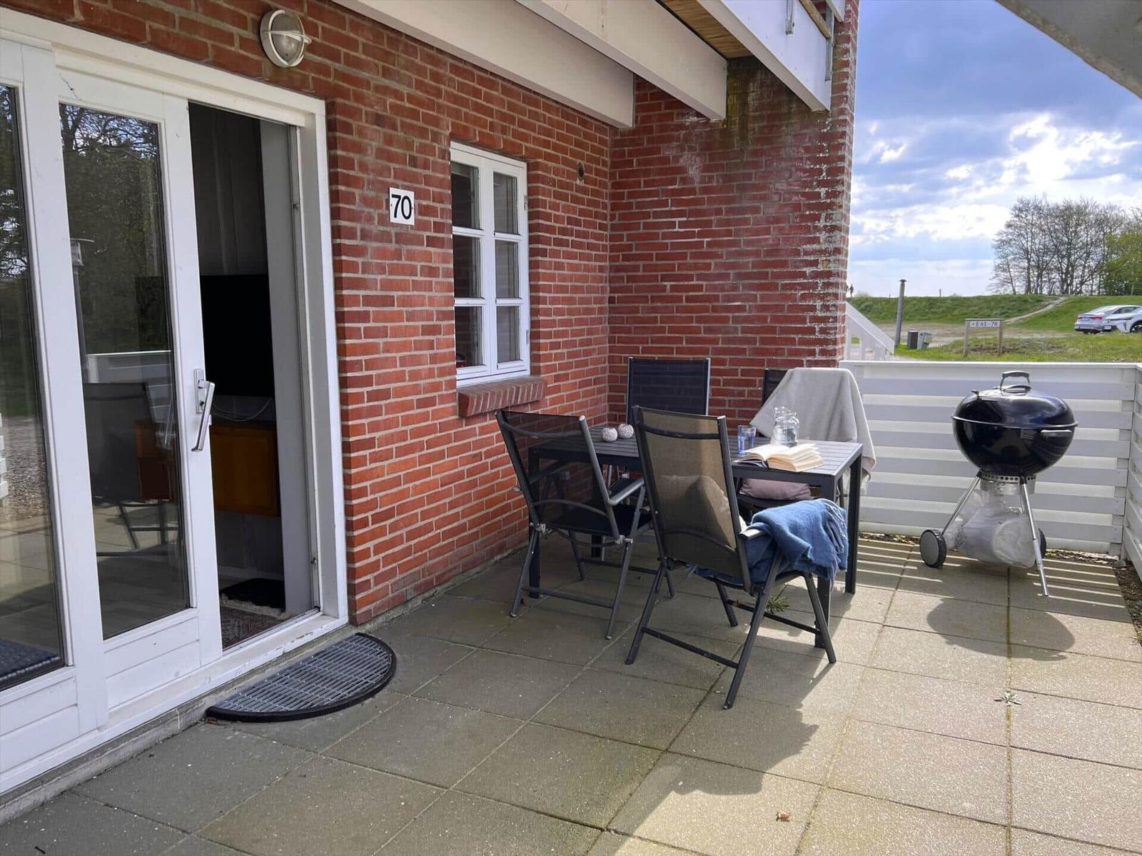 Terrasse mit Tisch, Stühlen und Grill neben rotem Backsteinhaus mit Eingangstür.