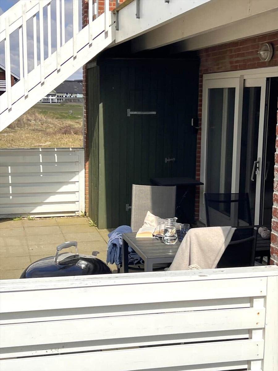 Terrasse mit Tisch, Stühlen und Grill. Hintergrund: Garten und Haus.