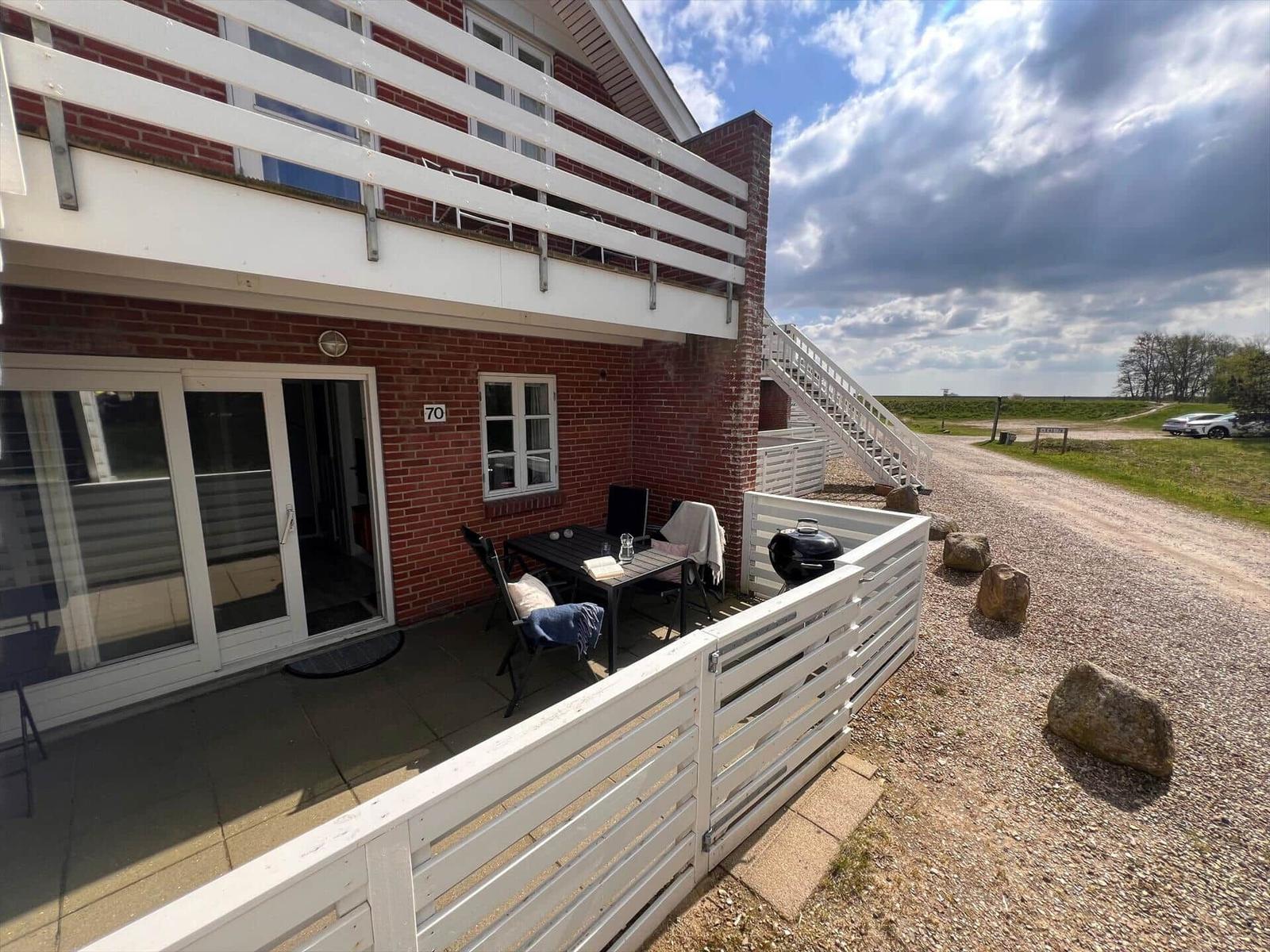 Rotes Backsteingebäude mit weißer Terrasse und Grill. Draußen Tisch, Stühle und Sicht auf Feld.