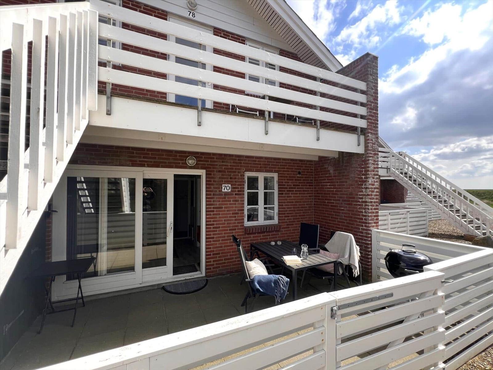 Terrasse mit Tisch, Stühlen und Grill. Hinterhof mit weißer Brüstung und rotem Backsteinhaus.