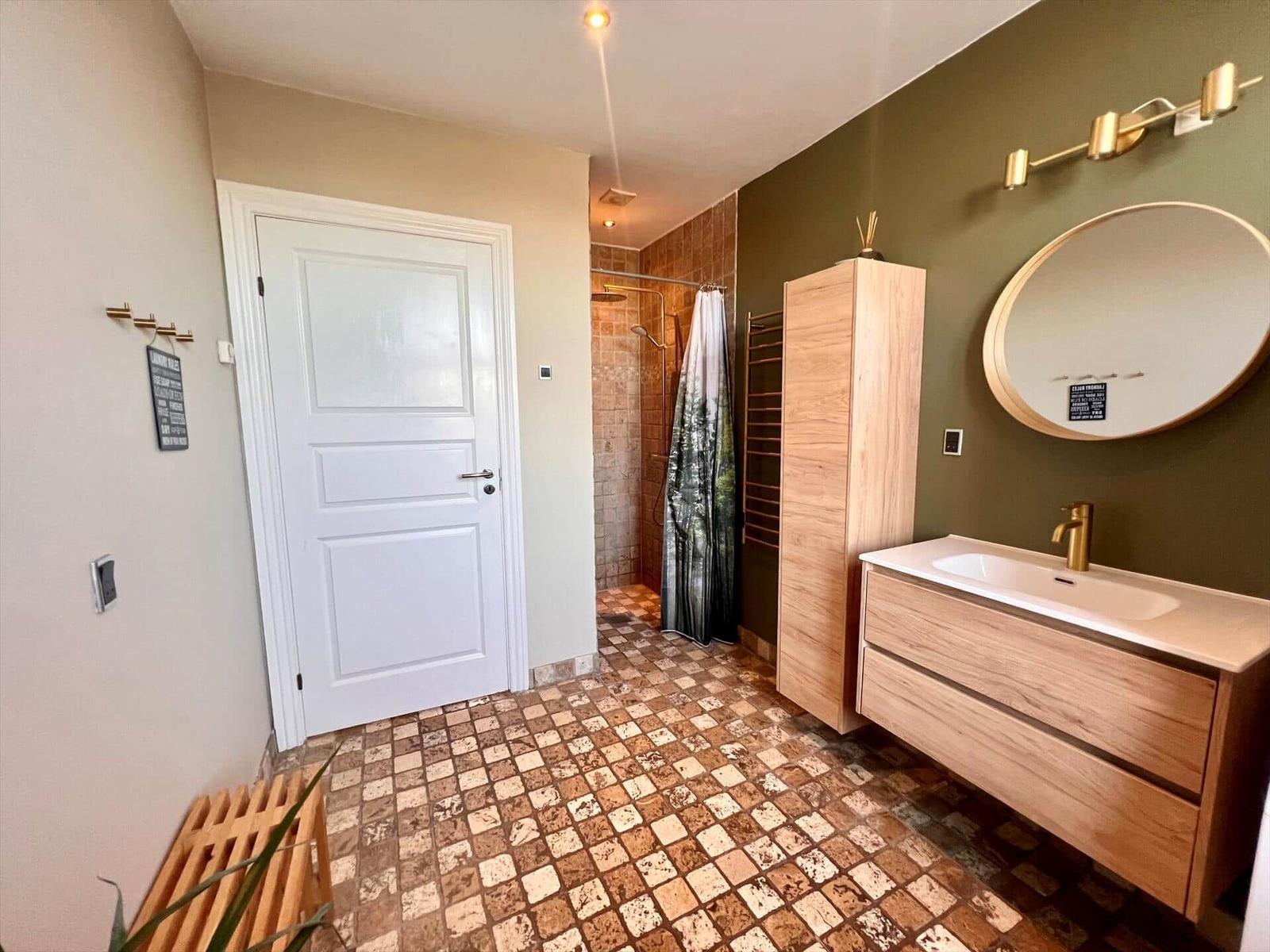 Badezimmer mit Holzwaschbecken, runden Spiegel und Dusche mit Vorhang.