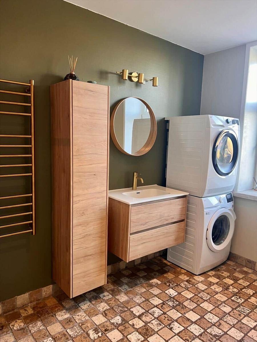 Badezimmer mit Waschmaschine und Trockner, Holzregal, runder Spiegel und Heizkörper.