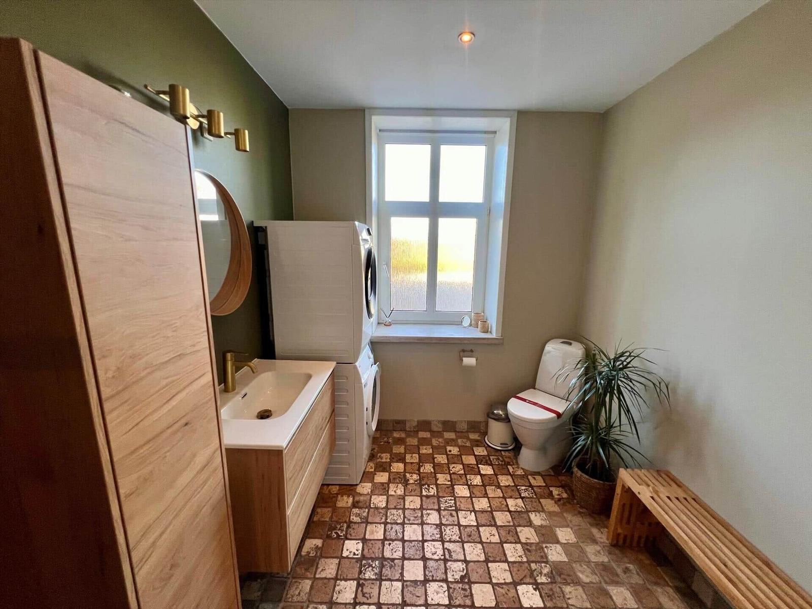 Bad mit Waschmaschine, Toilette, Pflanze und Holzbank.