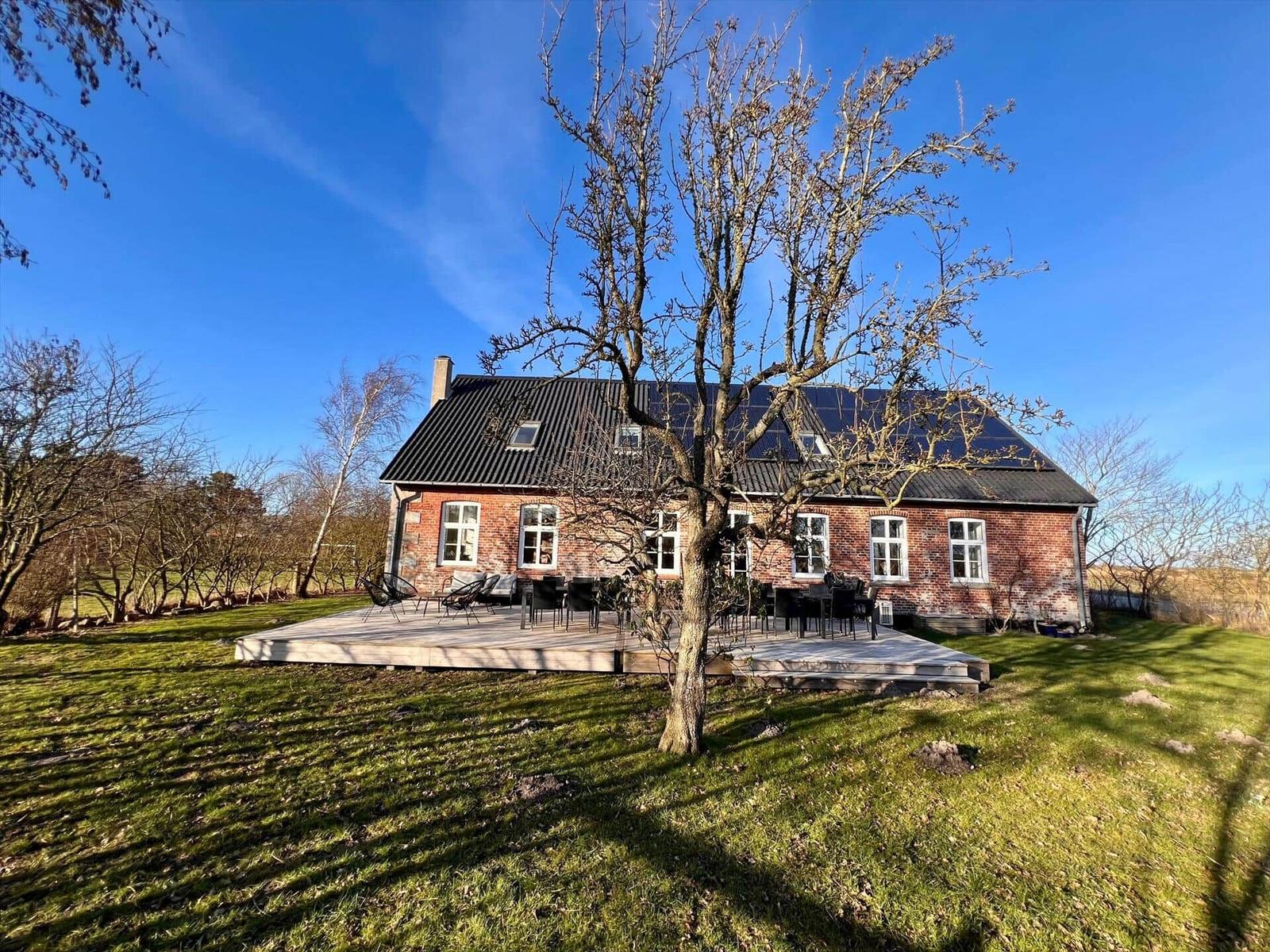 Rotes Backsteinhaus mit Terrasse und Solaranlage unter blauem Himmel.