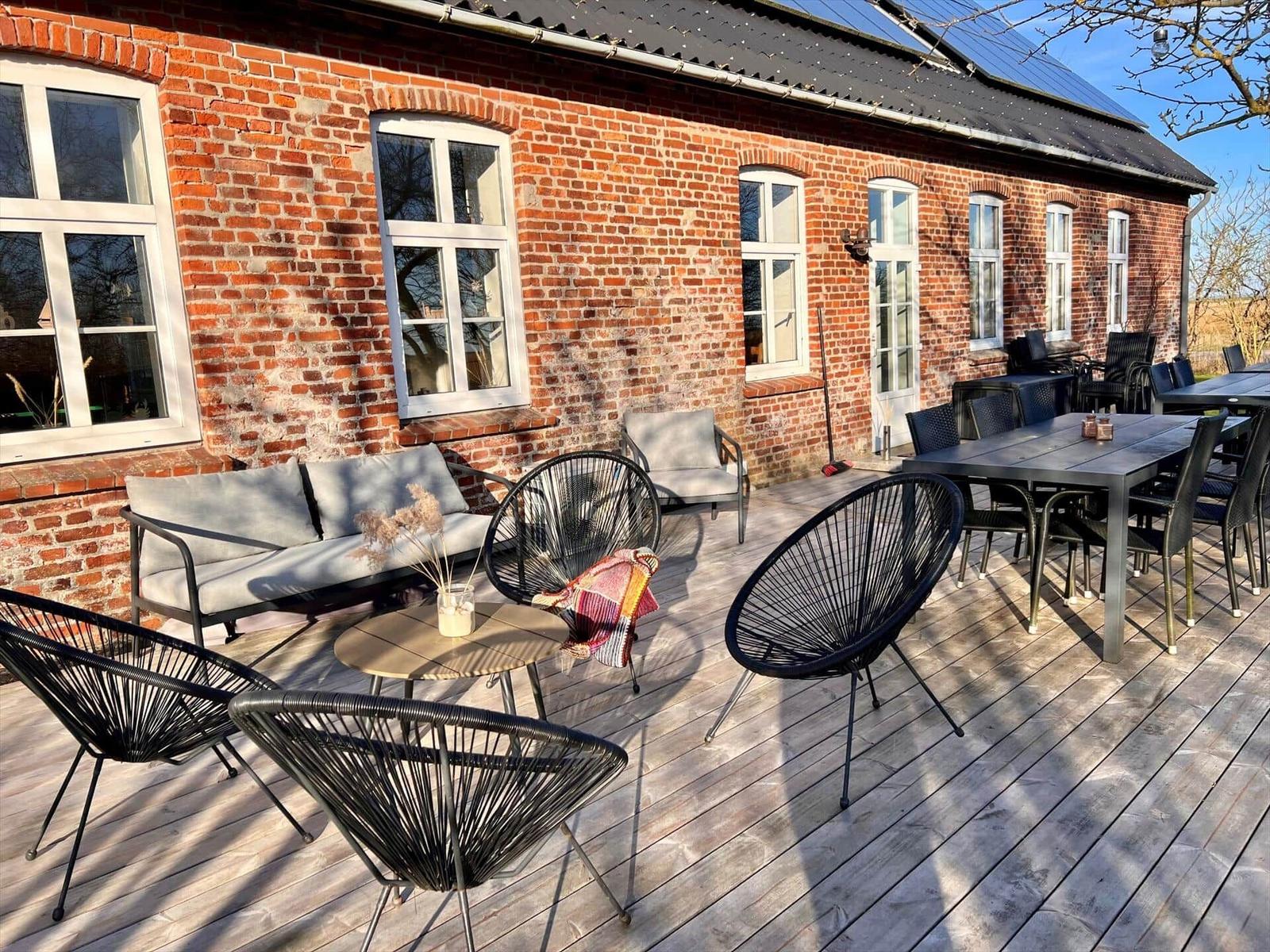 Terrasse mit Sitzgruppe und Tisch, vor rotem Backsteinhaus mit Fenstern.