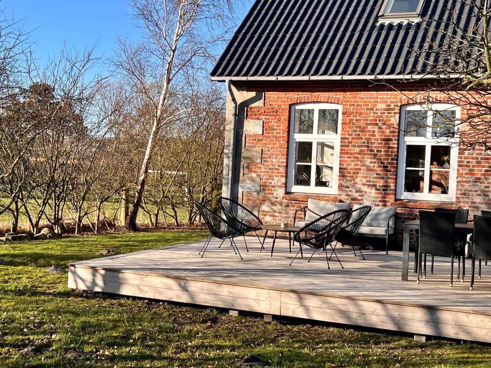 Holzterrasse mit Sitzgelegenheiten vor einem Backsteinhaus mit Dachfenster.
