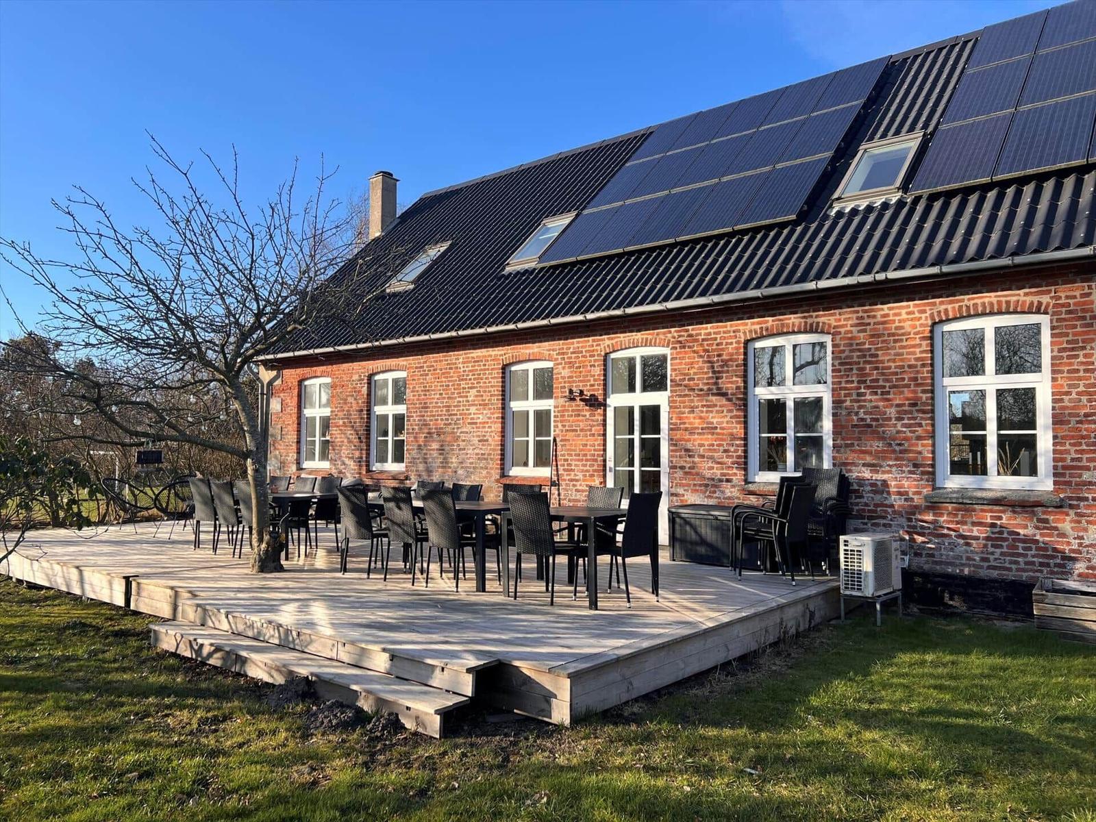Rotes Backsteinhaus mit Solaranlage und Terrasse mit Tischen und Stühlen.