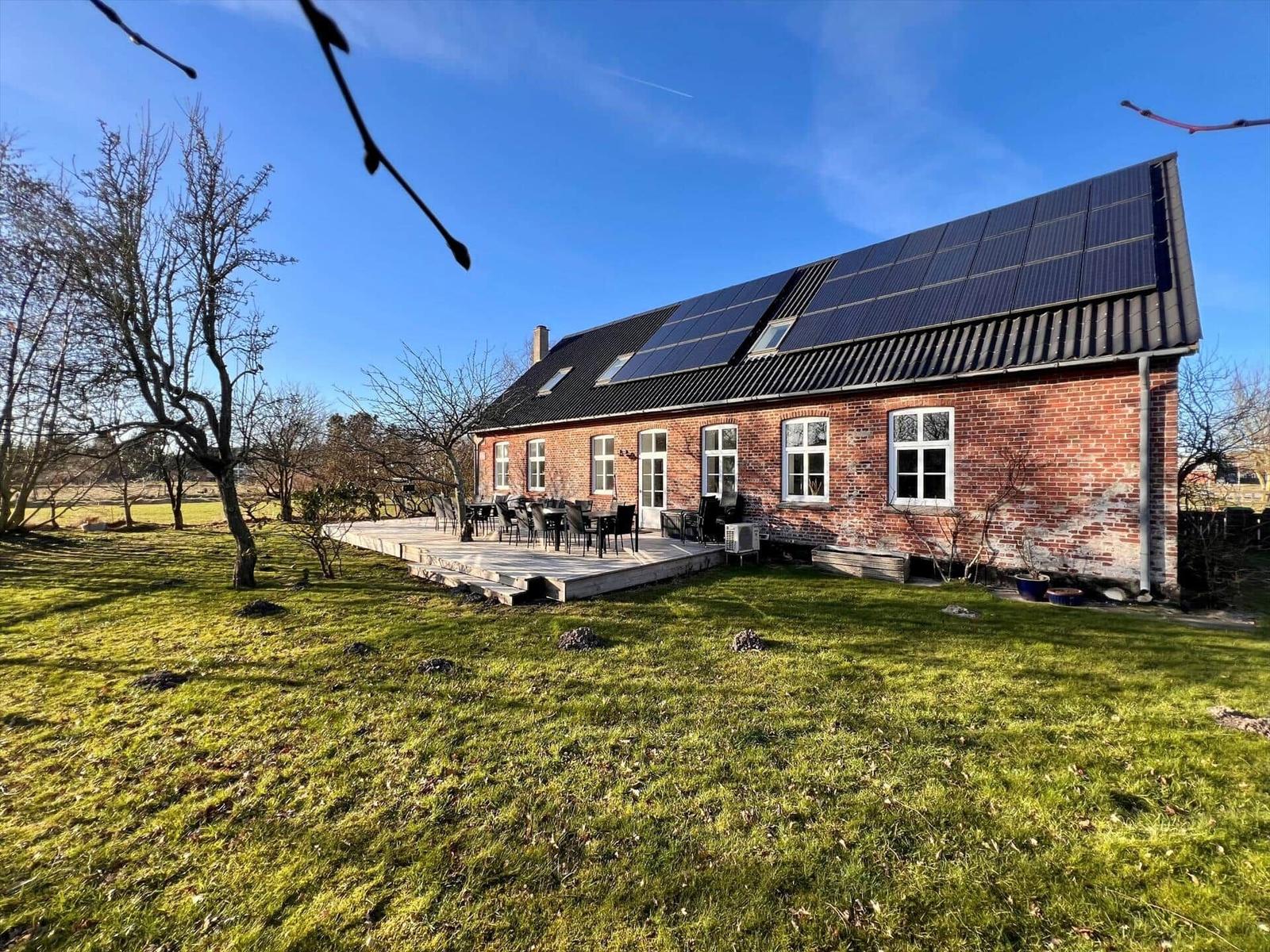 Rotes Backsteinhaus mit Solaranlage, Terrasse und Grünfläche.