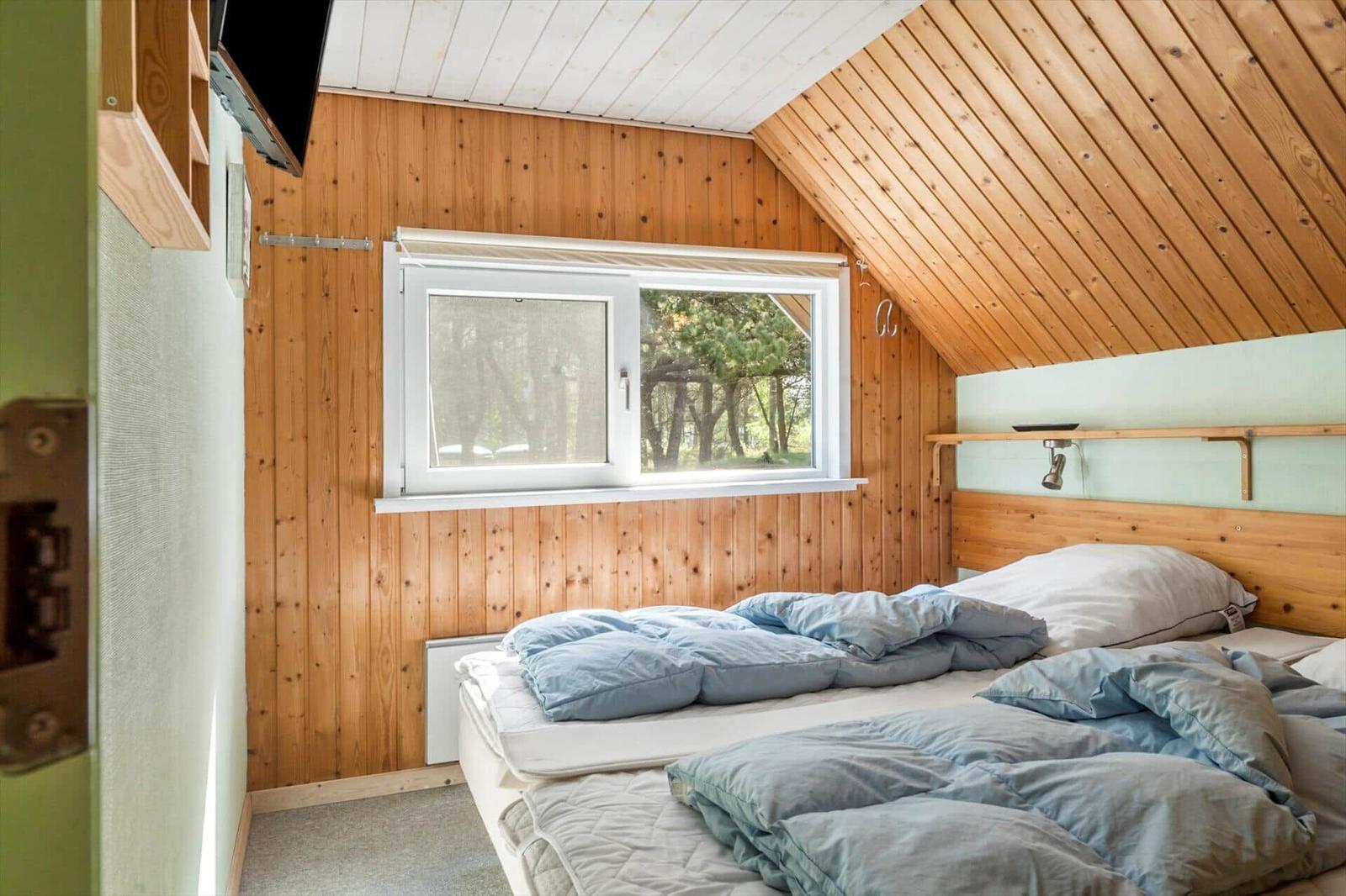 Schlafzimmer mit Holzwand, Fenster und Bett unter Dachschrägen.