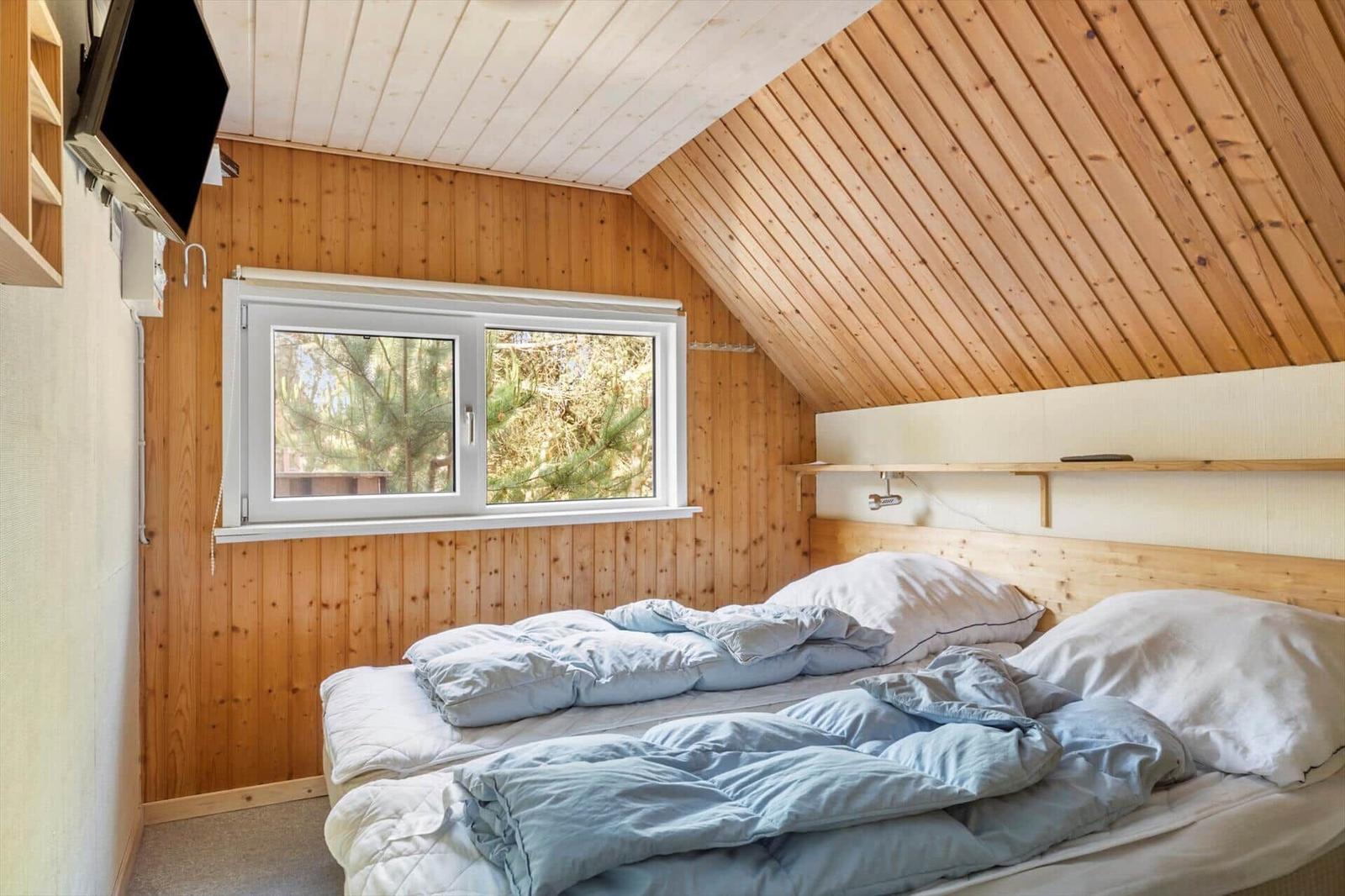 Schlafzimmer mit Holzwand, Dachboden und Fenster mit Blick auf Bäume.