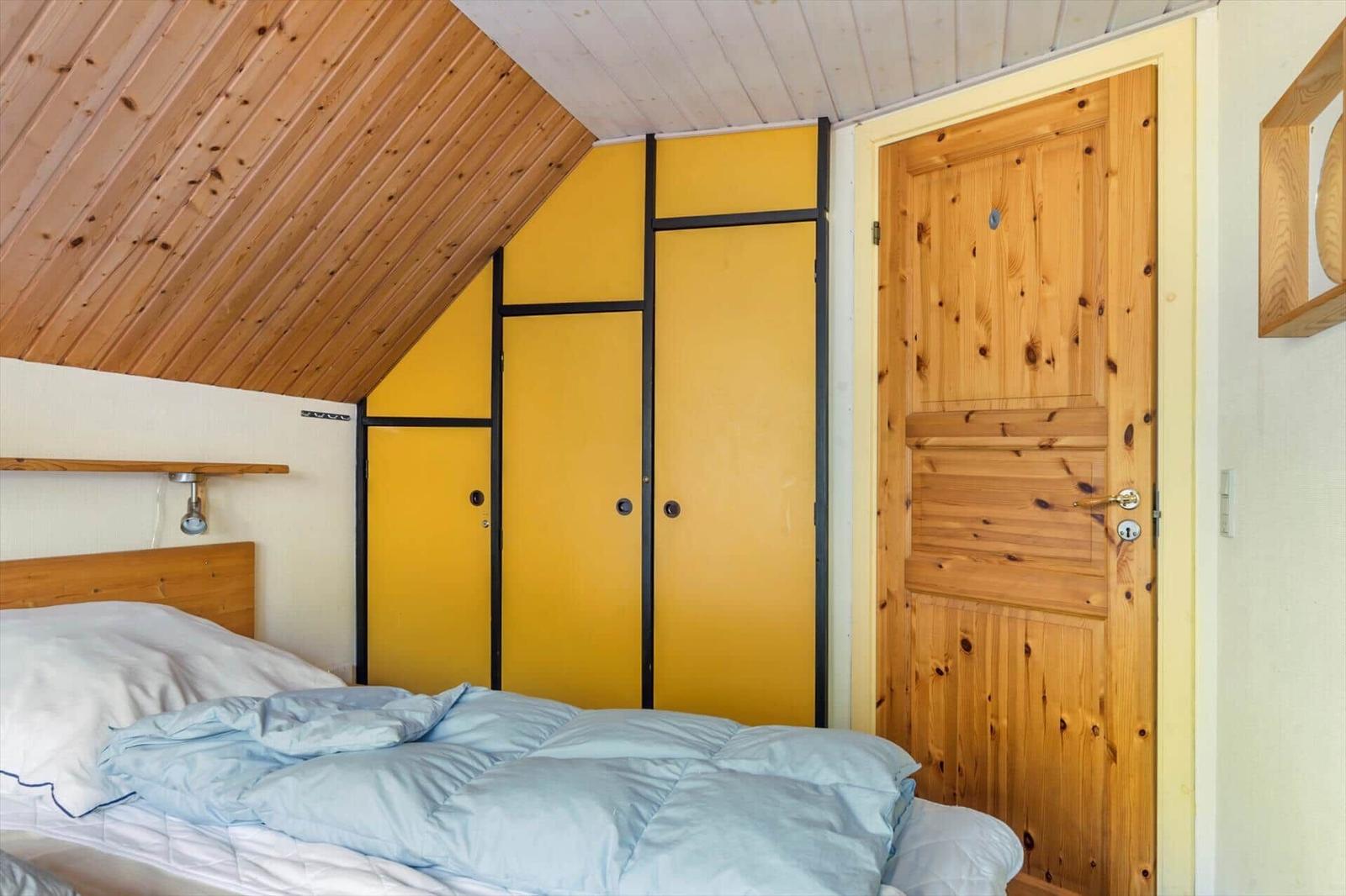 Schlafzimmer mit Holzdecke, gelbem Schrank und Holztür.