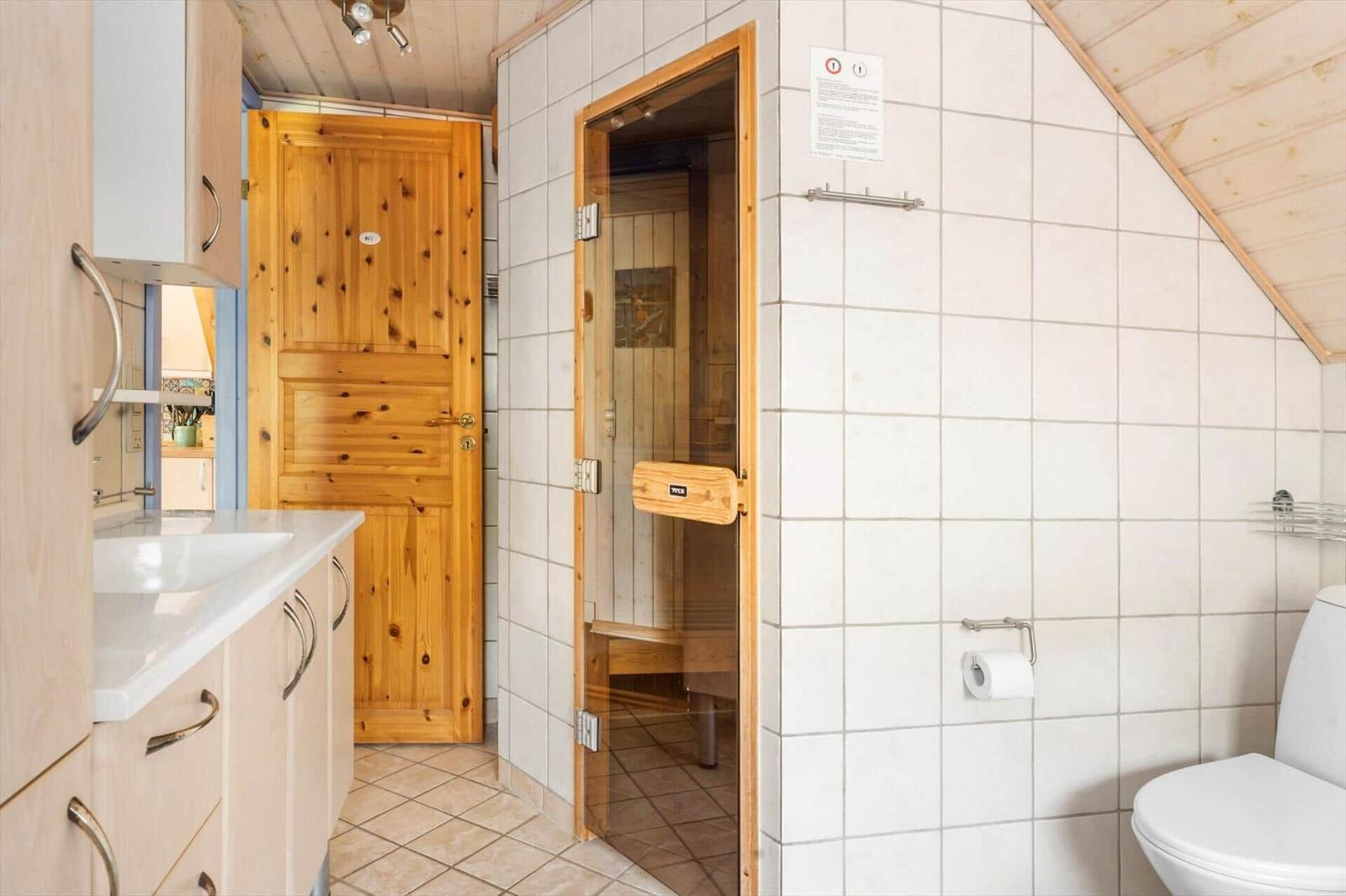 Bad mit Dusche, Toilette und Holztür zur Sauna