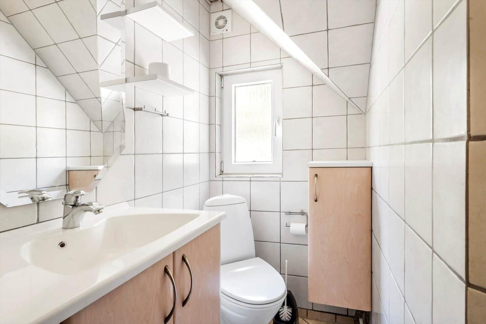 Badezimmer mit Waschbecken, Toilette und Fenster unter Dachschrägen.
