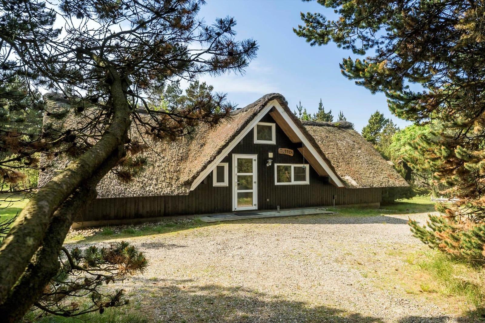 Dorfhaus mit Strohdach und Holzfassade unter Bäumen