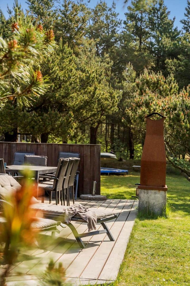 Terrasse mit Liegen und Tisch im Grünen, umgeben von Bäumen und Gras.