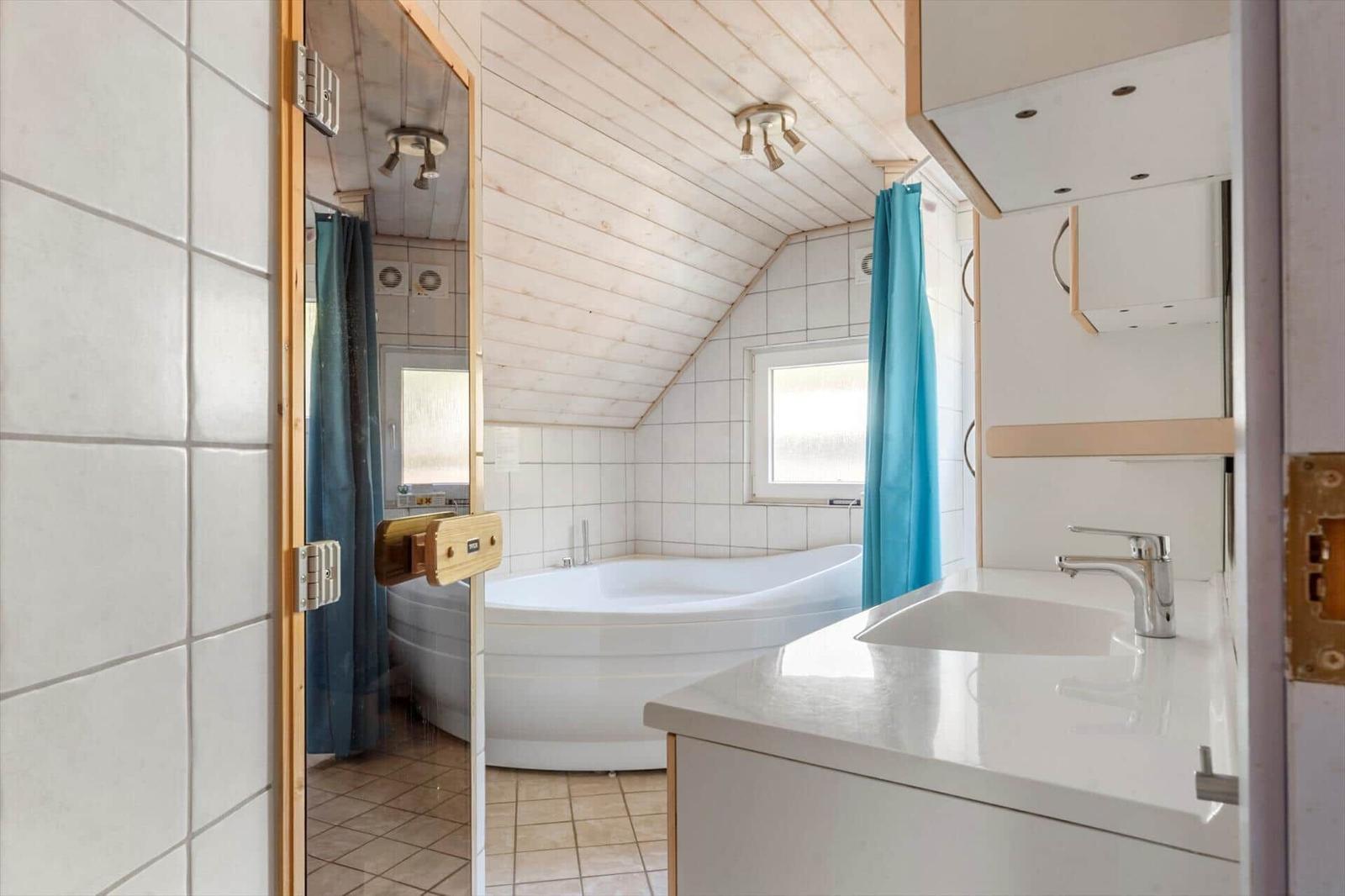 Badezimmer mit Badewanne, Waschbecken und Spiegel. Holzdecke und blaue Vorhänge.