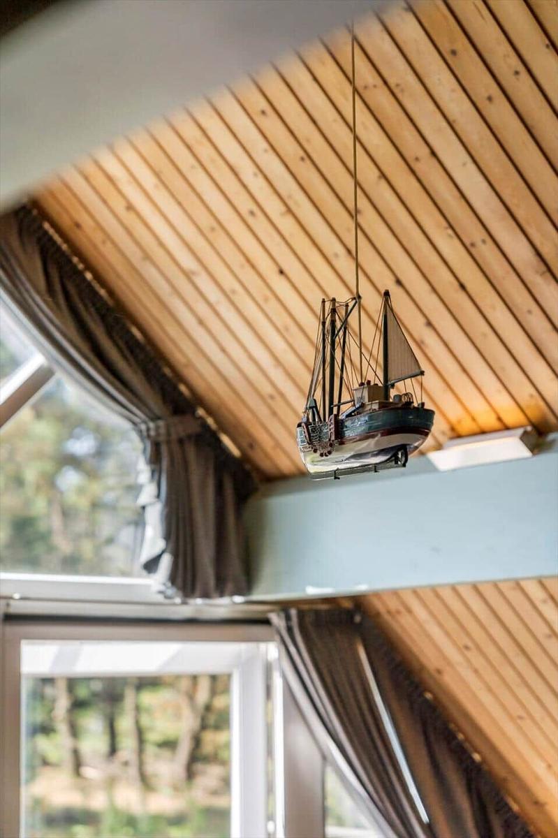Ein kleines Segelschiff hängt von der Holzdecke. Durch Fenster ist Wald zu sehen.