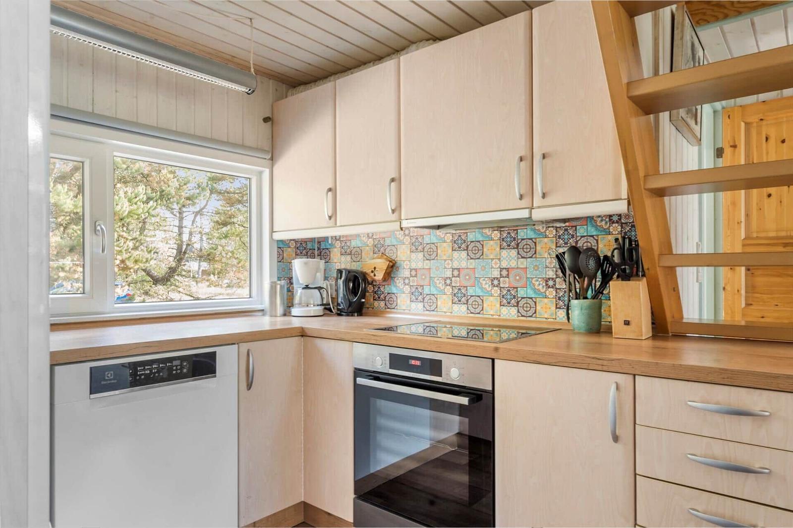 Küche mit Holzschränken, Fenster und farbiger Fliese im Hintergrund.