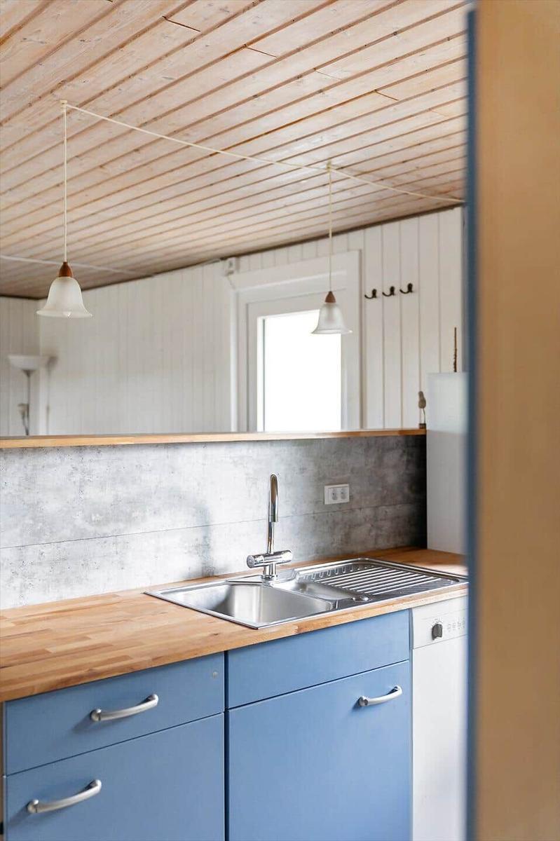 Küche mit blauen Schränken, Holzoberfläche und Edelstahlspüle unter Holzdecke.