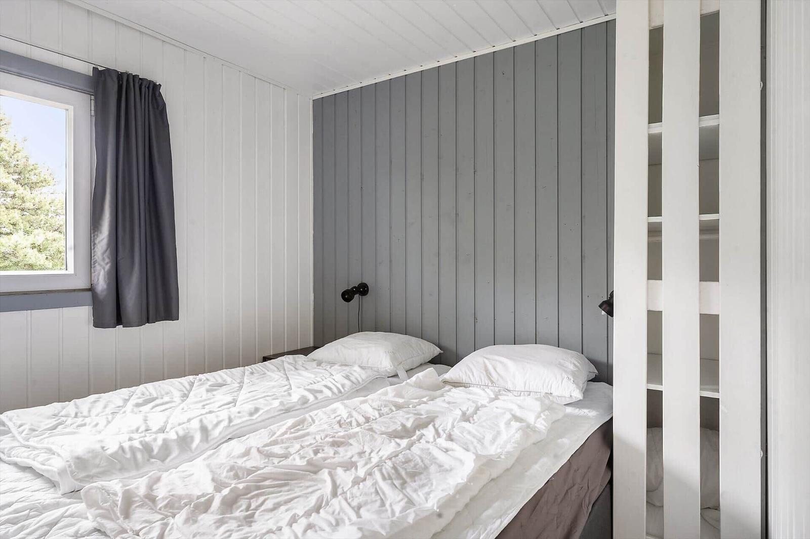 Schlafzimmer mit Bett, Fenster und Kleiderschrank. Wände sind weiß und grau verkleidet.