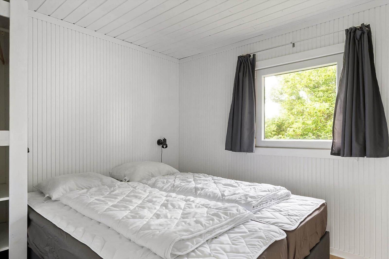 Schlafzimmer mit Doppelbett, weißen Wänden und Fenster mit Blick auf Bäume.