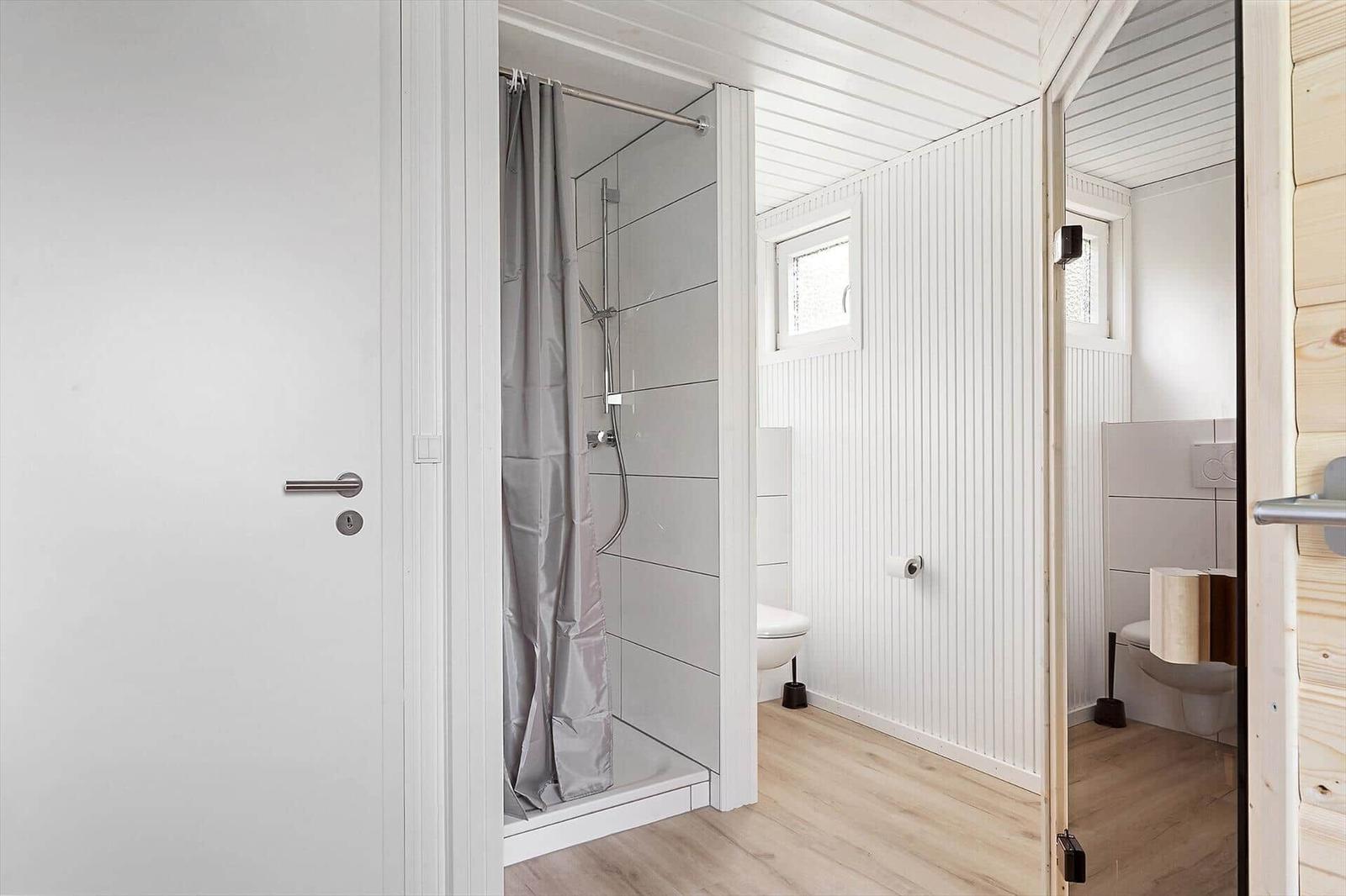 Badezimmer mit Dusche, Toilette und Fenster. Holzfußboden und weiße Wände.