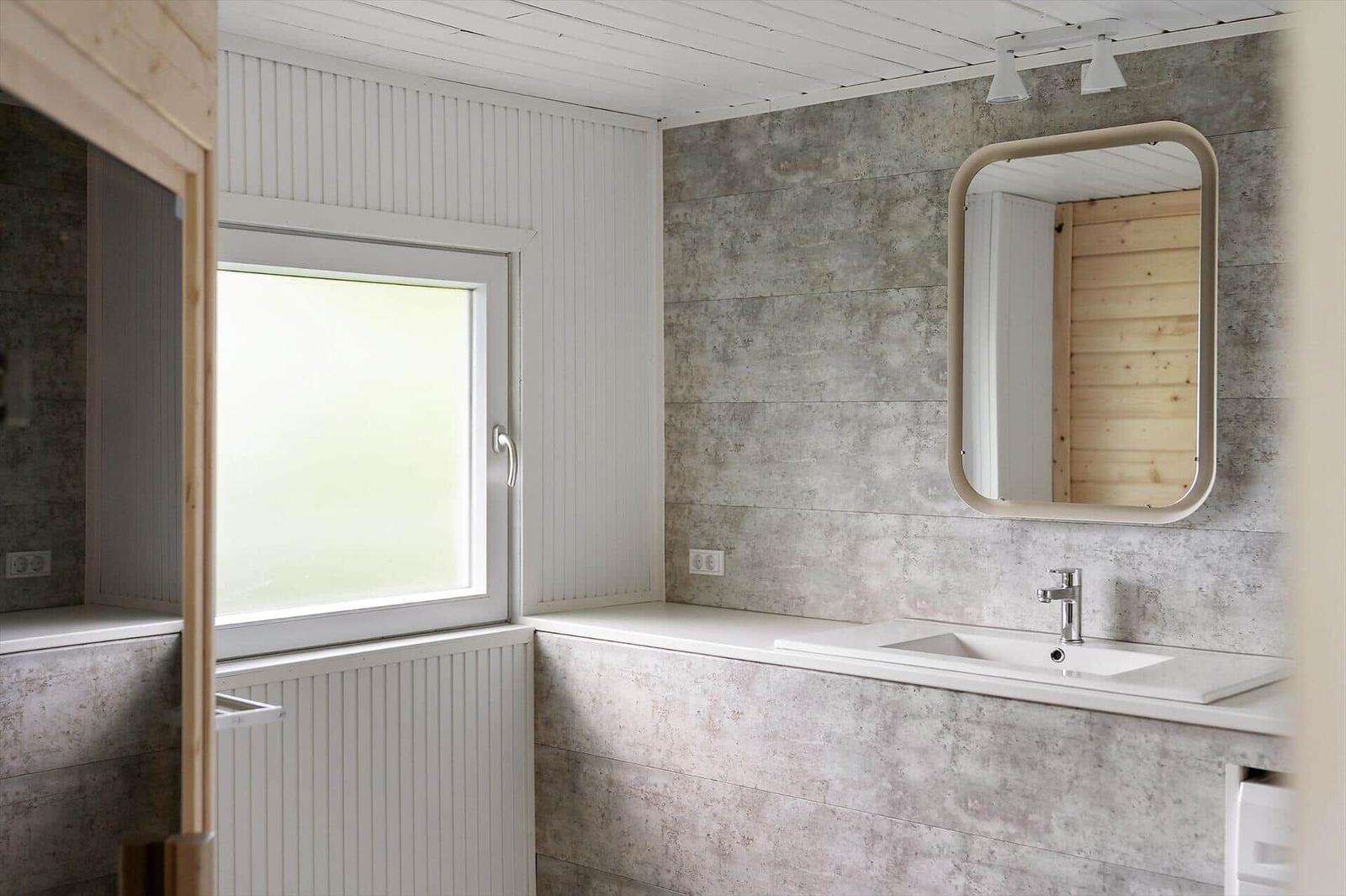 Badezimmer mit Waschbecken, Spiegel und Fenster. Wandverkleidung aus Betonoptik und Holz.