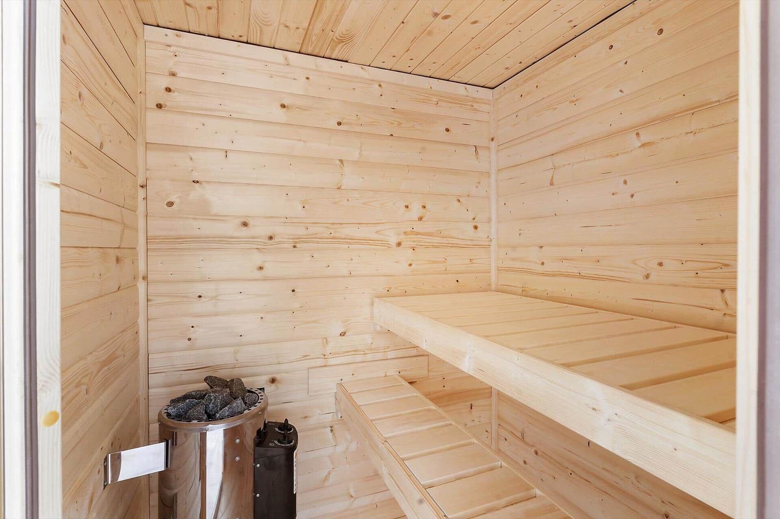 Sauna mit Holzwand und mehreren Bänken sowie einem Ofen mit Steinen.