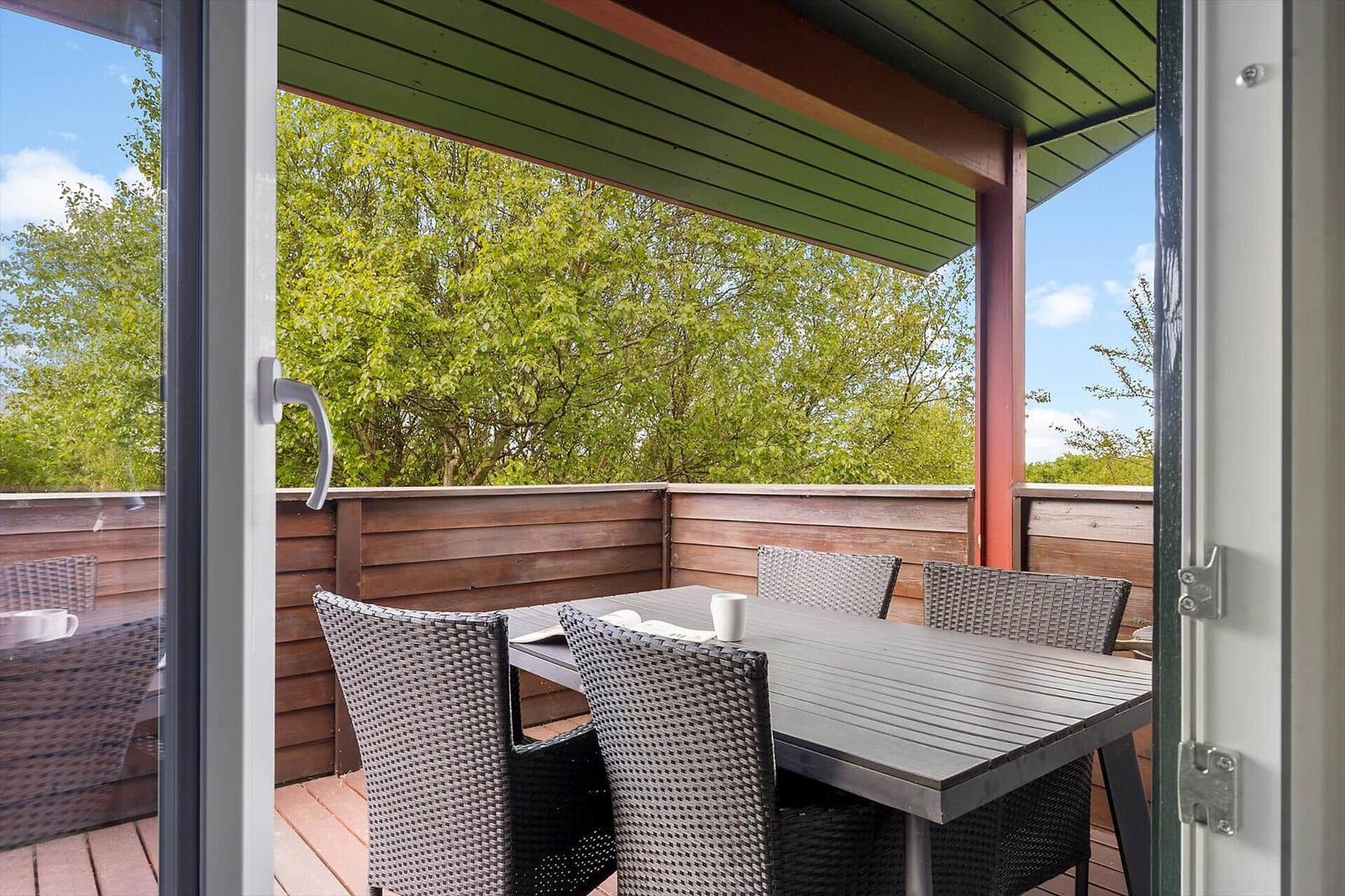 Terrasse mit Tisch und Stühlen, umgeben von Bäumen unter einem grünen Dach.