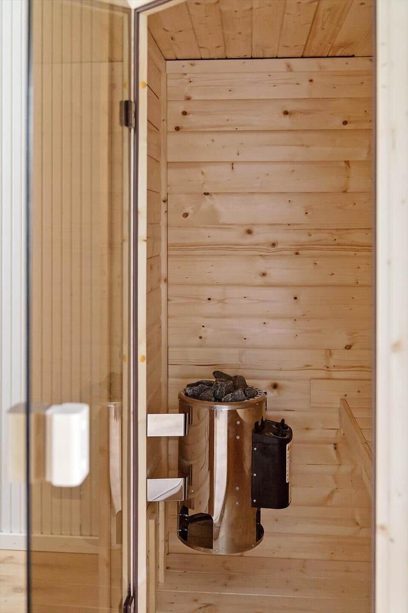 Sauna mit Holzwand und Edelstahlheizung mit Steinen.