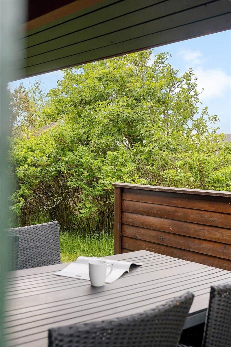 Terrasse mit Tisch, Stühlen und Tasse. Blick auf grüne Hecke und Himmel.