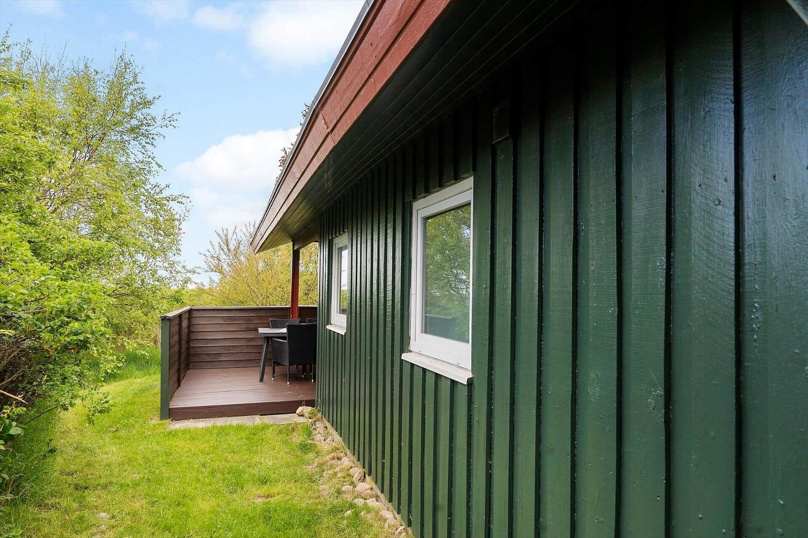Grünes Holzhaus mit Terrasse und Garten. Weiße Fenster und Holzveranda.