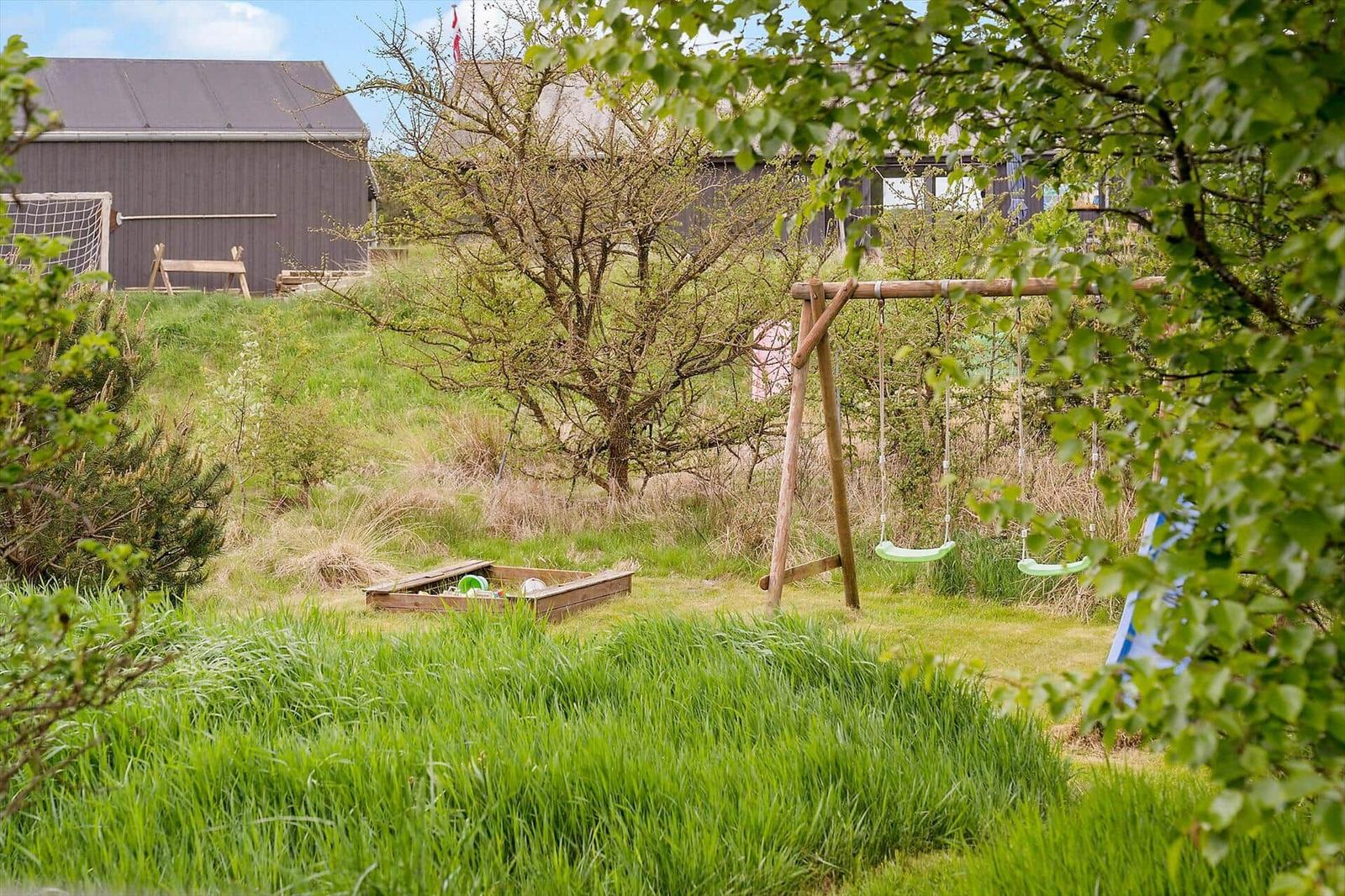 Grüner Garten mit Schaukel, Spielplatz und Holzhaus im Hintergrund.