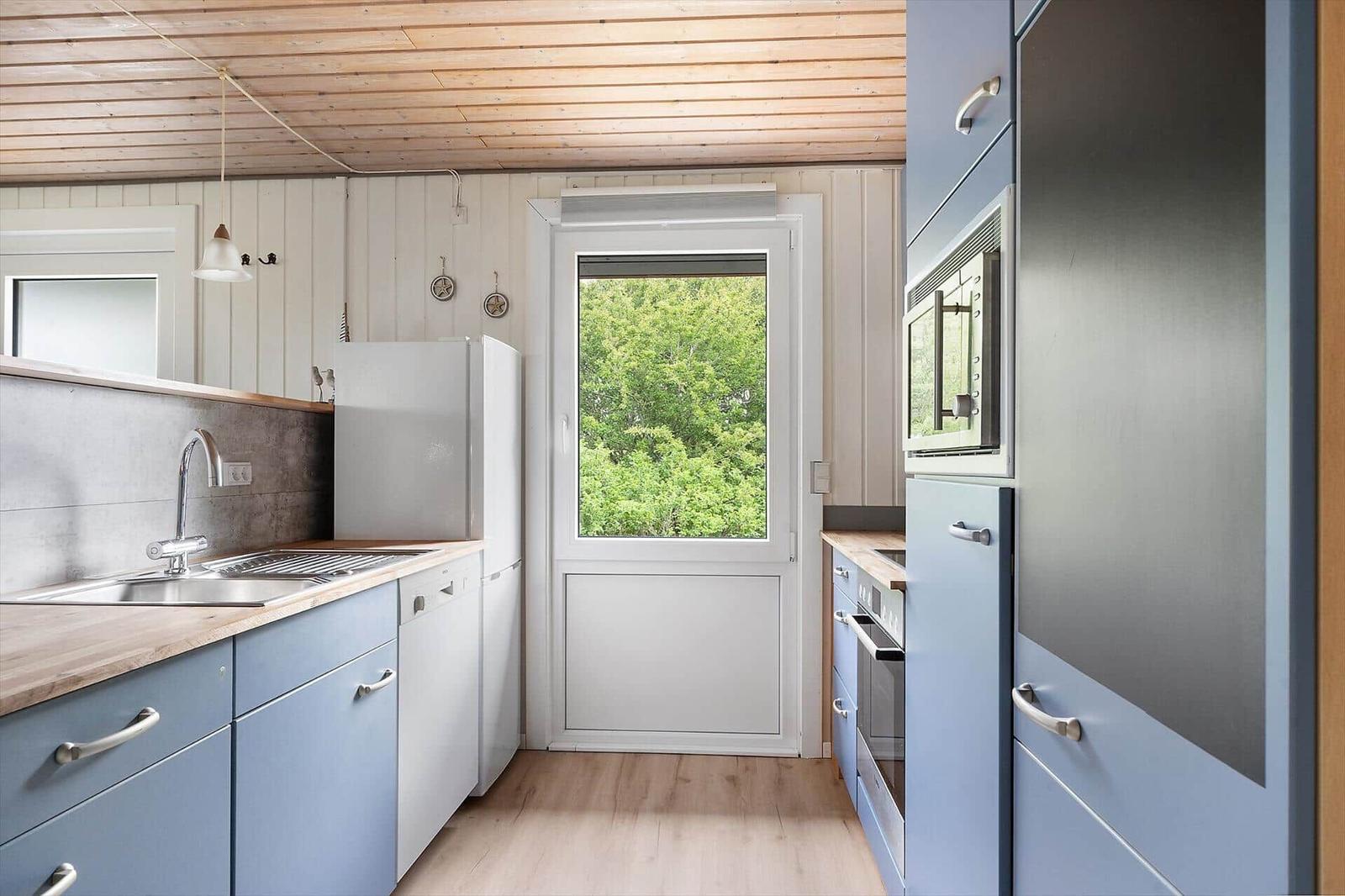 Küche mit blauen Schränken, Holzboden und Fenster zum Grün.