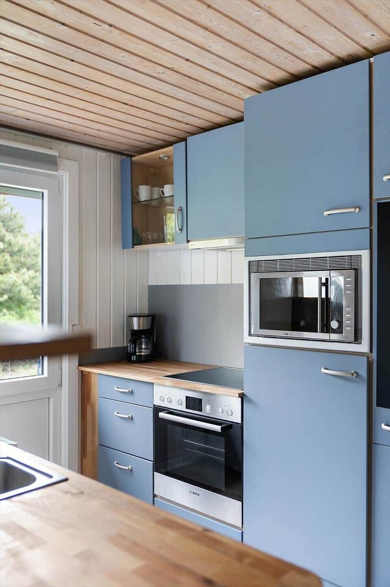 Küche mit blauen Schränken, Holzoberfläche und eingebauter Mikrowelle und Backofen.