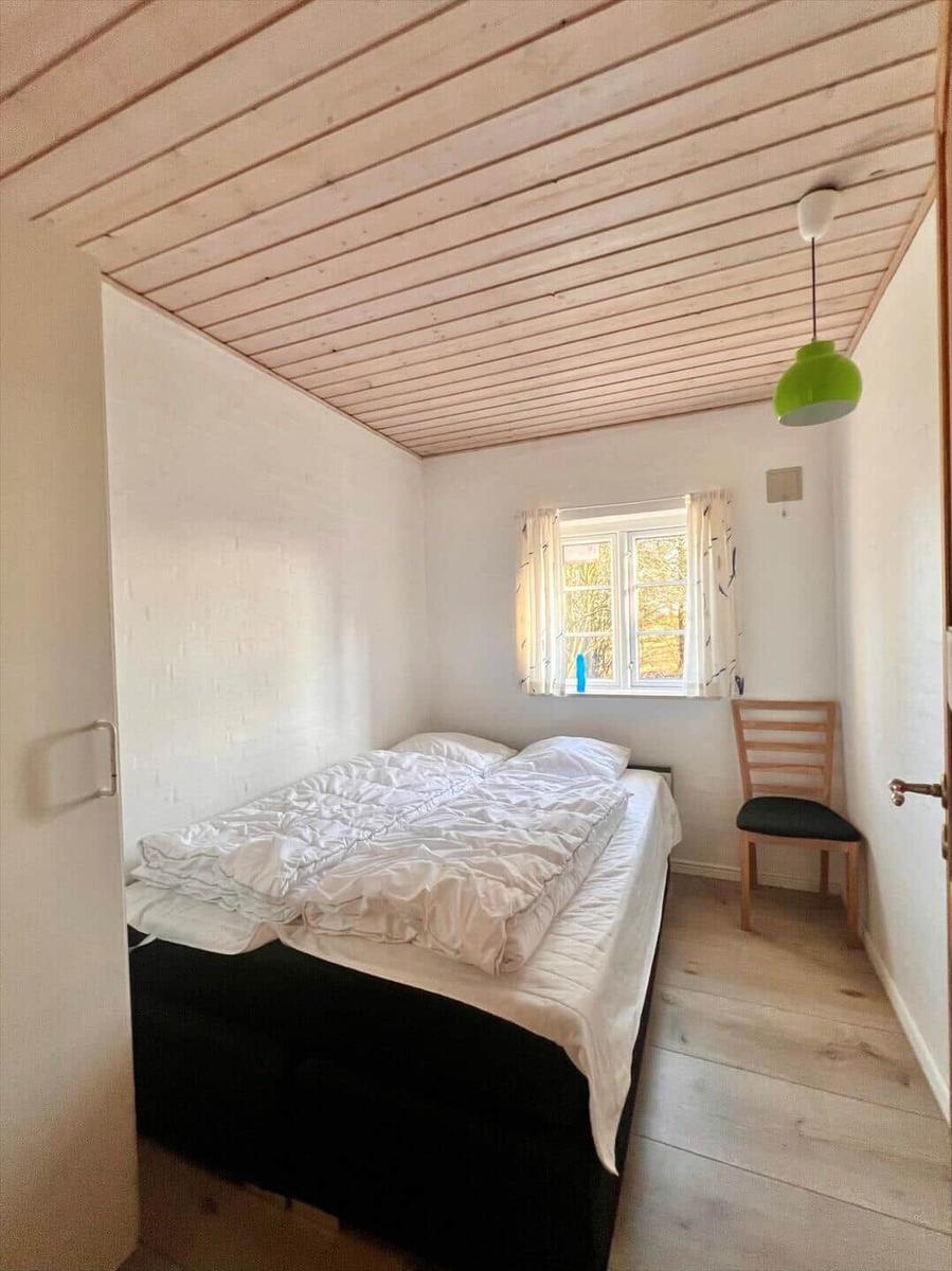 Schlafzimmer mit Bett, Stuhl und Fenster. Holzdecke und -boden.
