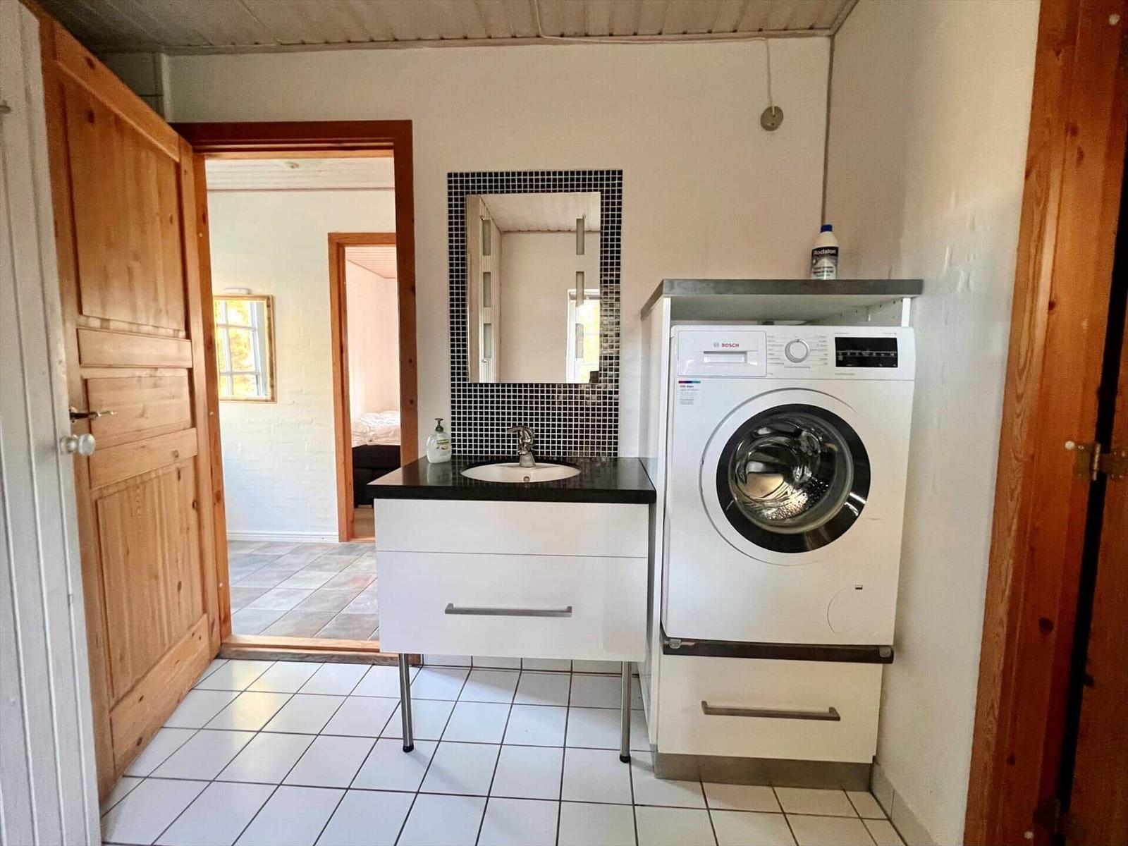 Waschmaschine und Waschbecken mit Spiegel in einem Raum mit Fliesenboden und Holztüren.