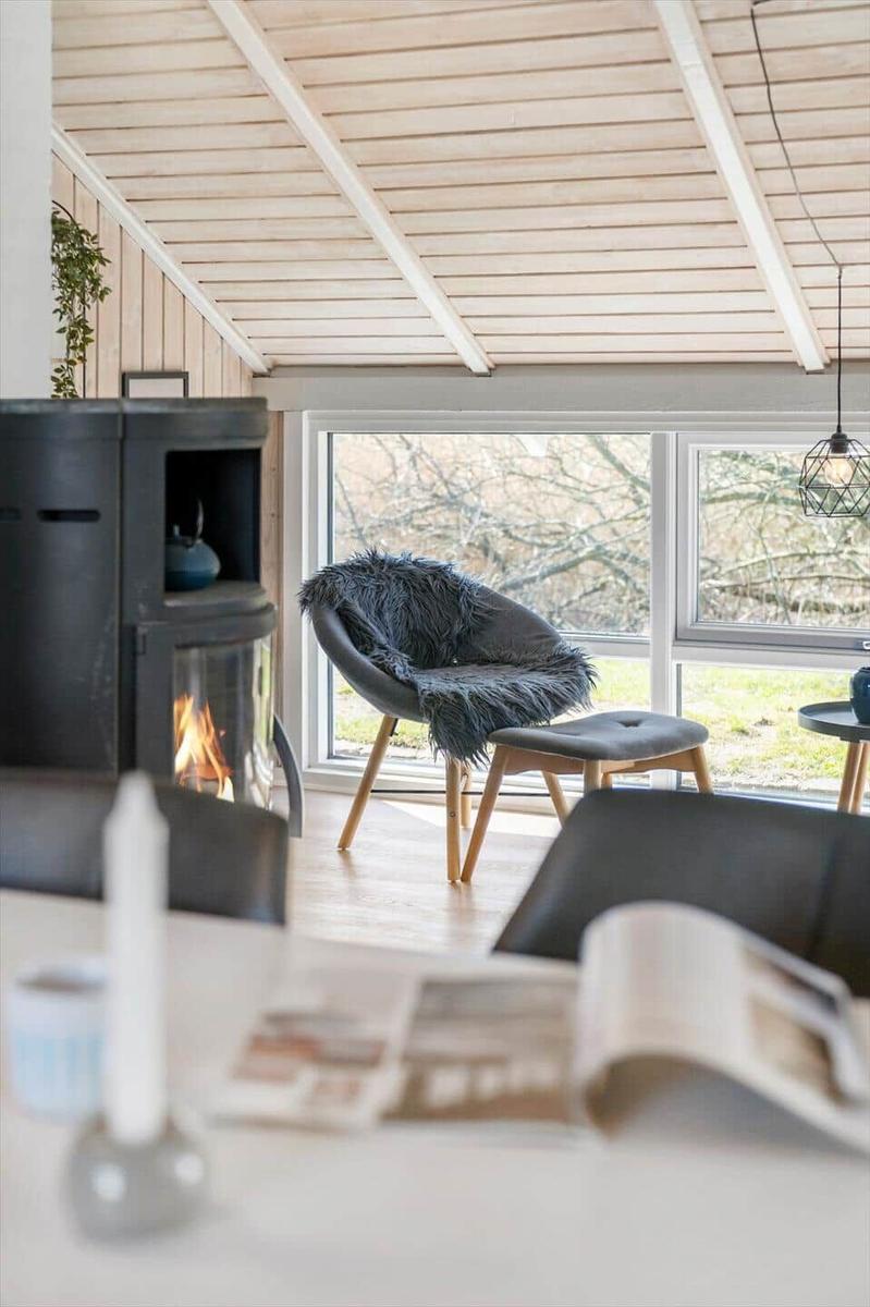 Ein Raum mit Holzdecke, Kamin und Sessel vor großem Fenster.