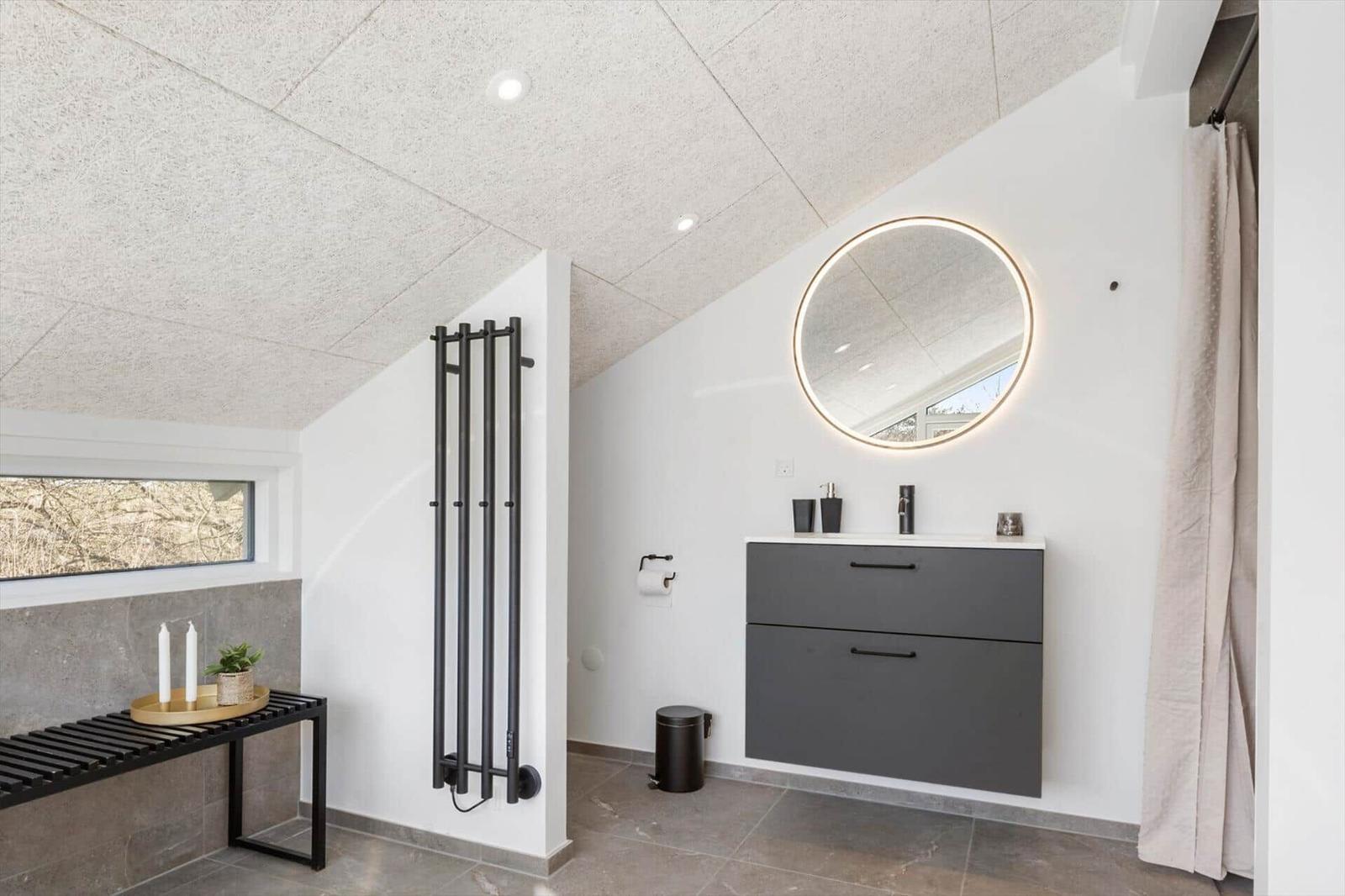 Moderne Badezimmer mit runden Spiegel, grauem Waschtisch und Fenster.