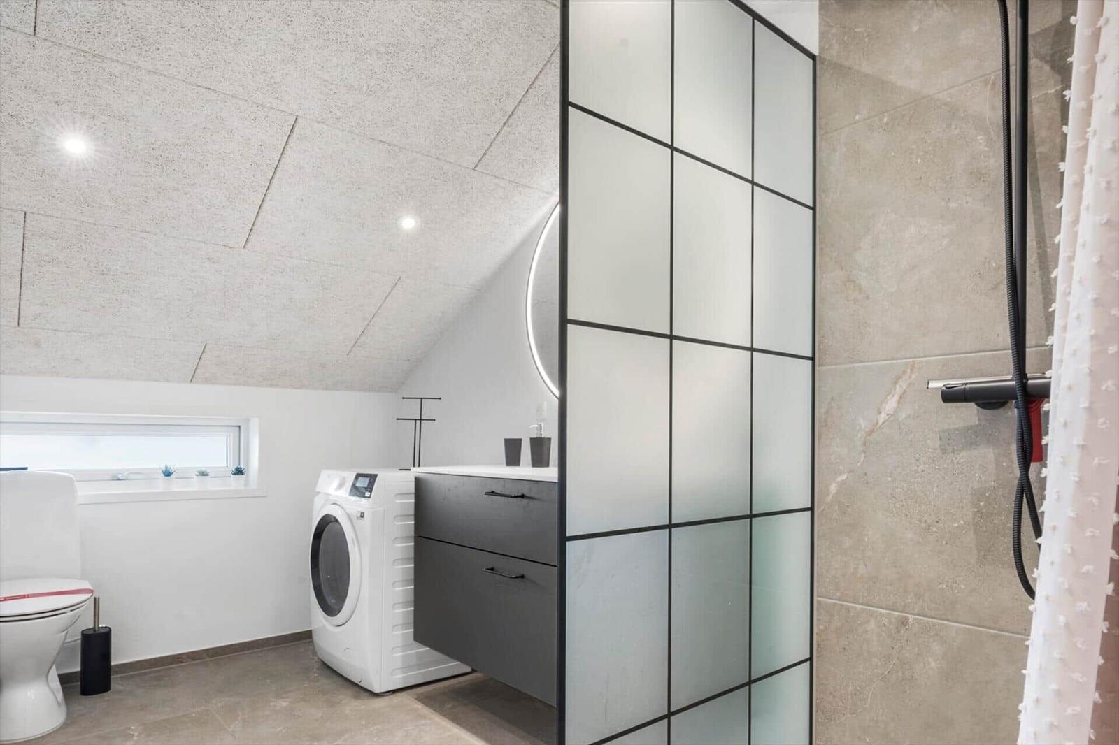 Badezimmer mit Dusche, Waschmaschine und Toilette unter Dachschrägen.