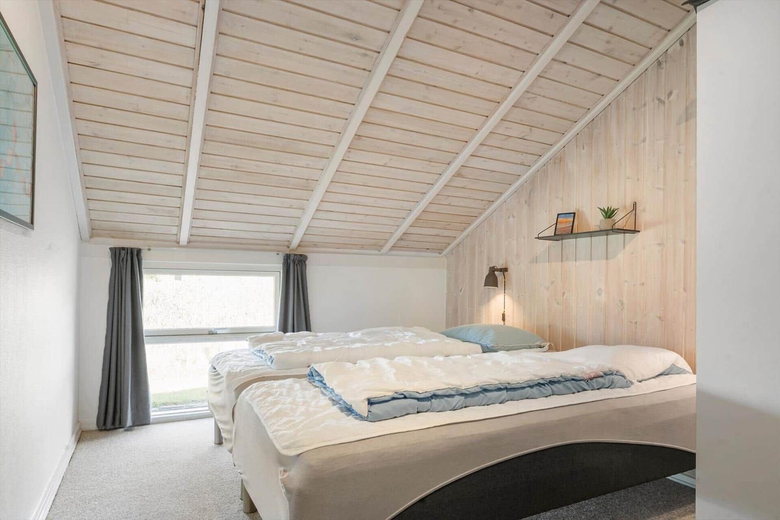 Zwei Betten in einem Raum mit Holzwand und -decke. Fenster mit grauen Vorhängen.