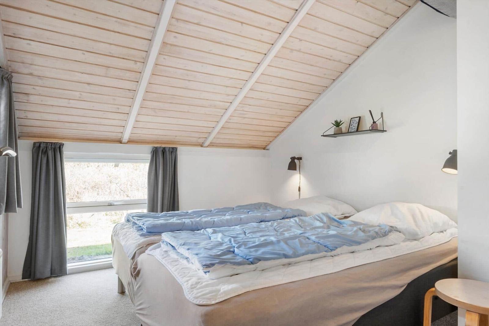 Schlafzimmer mit Bett, Fenster und Holzdecke.
