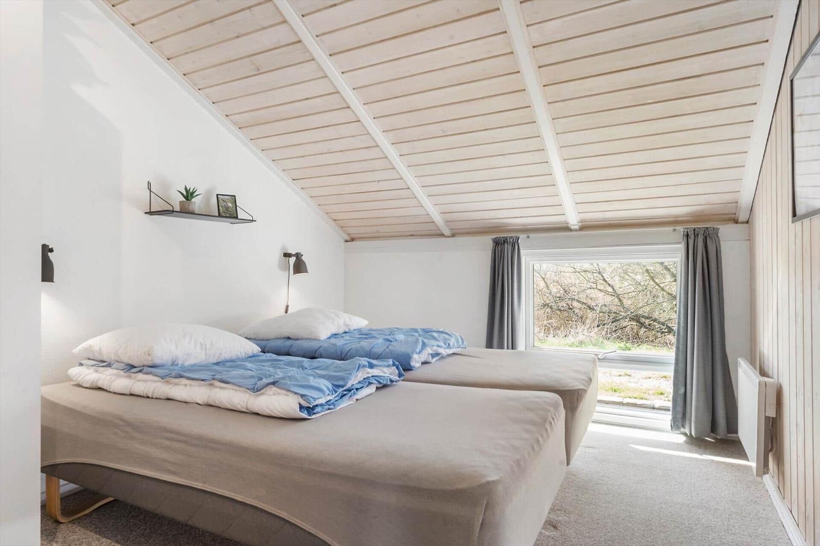 Zwei Betten unter einem Holzdach mit Fenster und grauen Vorhängen.