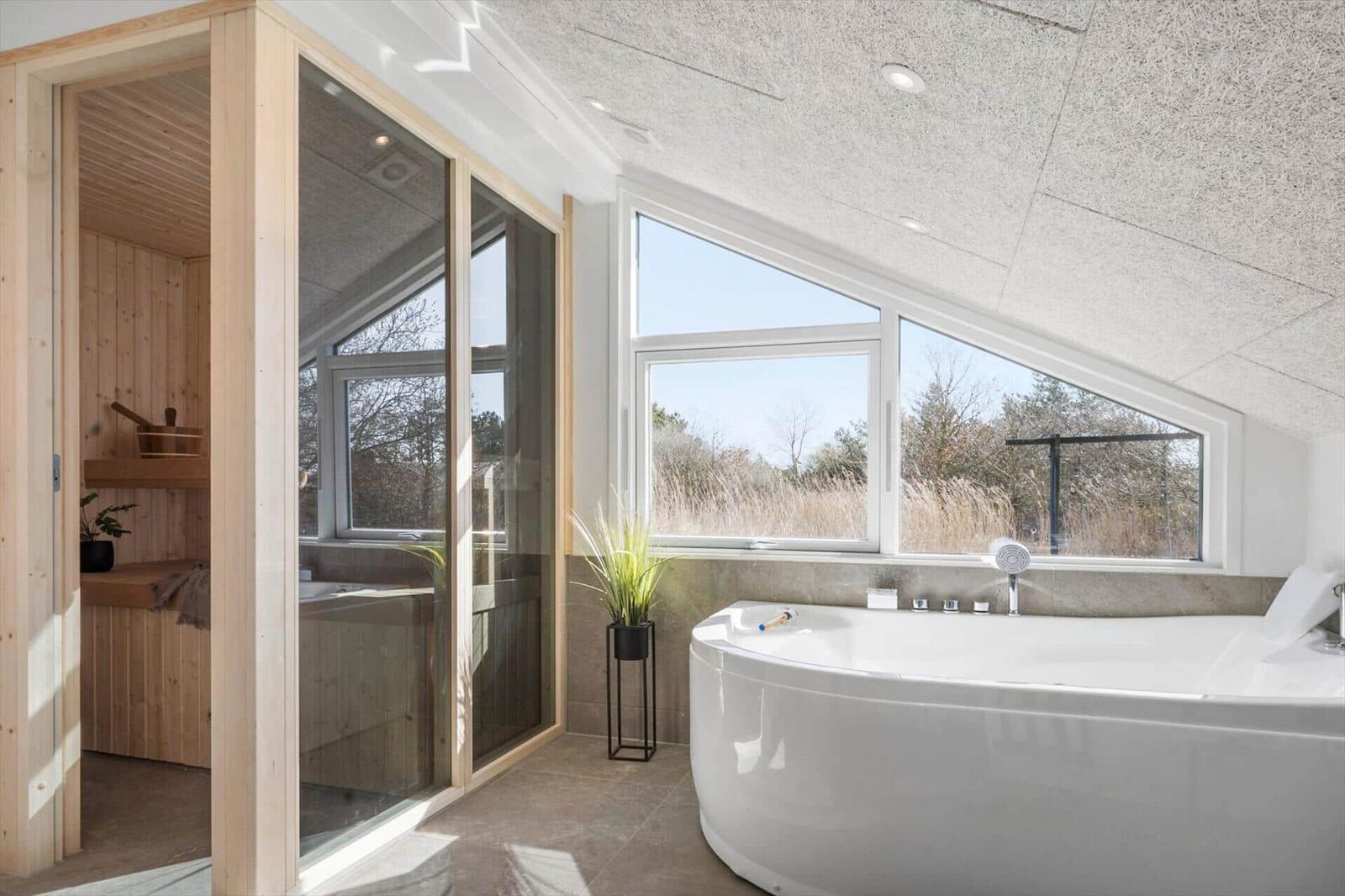 Bad mit freistehender Badewanne und Sauna im Hintergrund.
