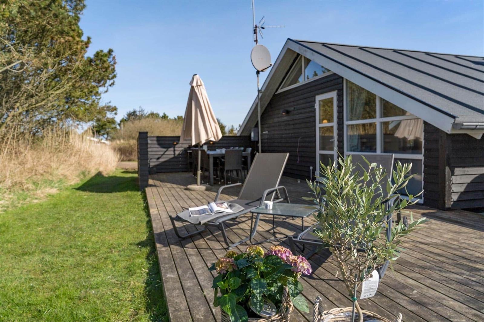 Terrasse mit Liege, Tisch und Sonnenschirm neben einem Holzhaus mit Satellitenantenne.