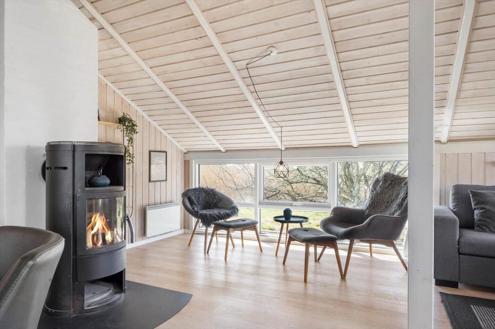 Wohnraum mit Kamin, Sitzgelegenheiten und großem Fenster. Holzdecke und -boden.